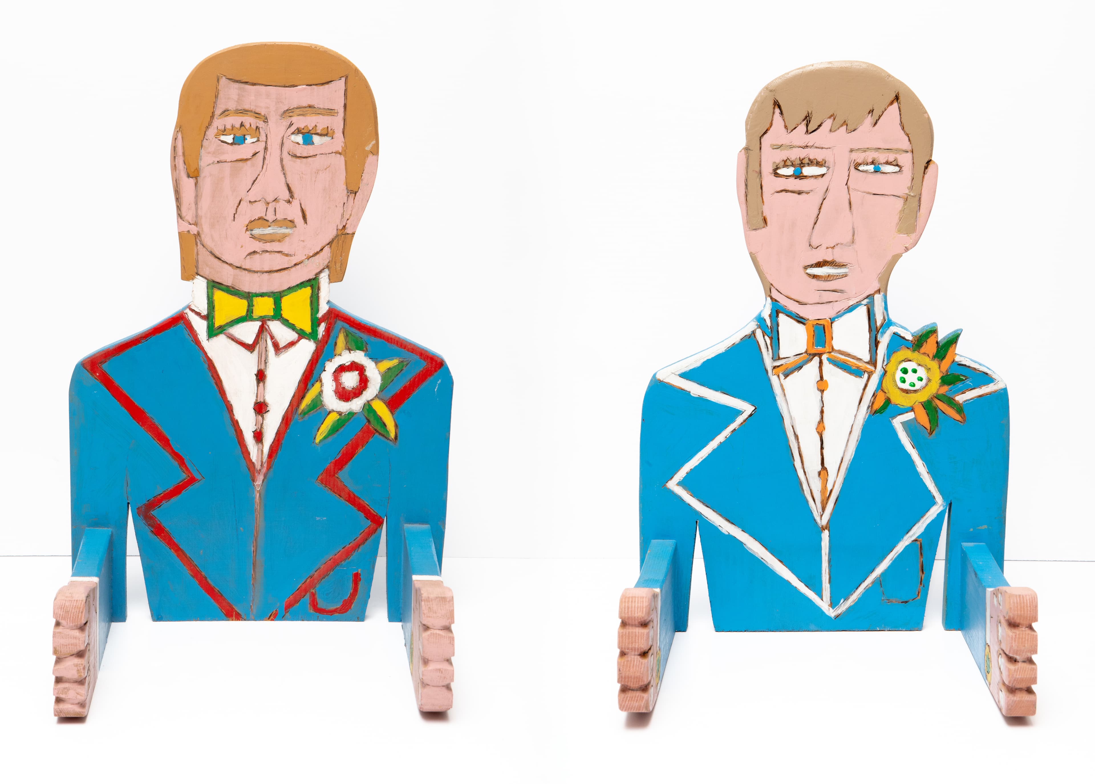 Two painted wooden sculptures of figures in blue suits with decorative medals, mounted on wooden posts
