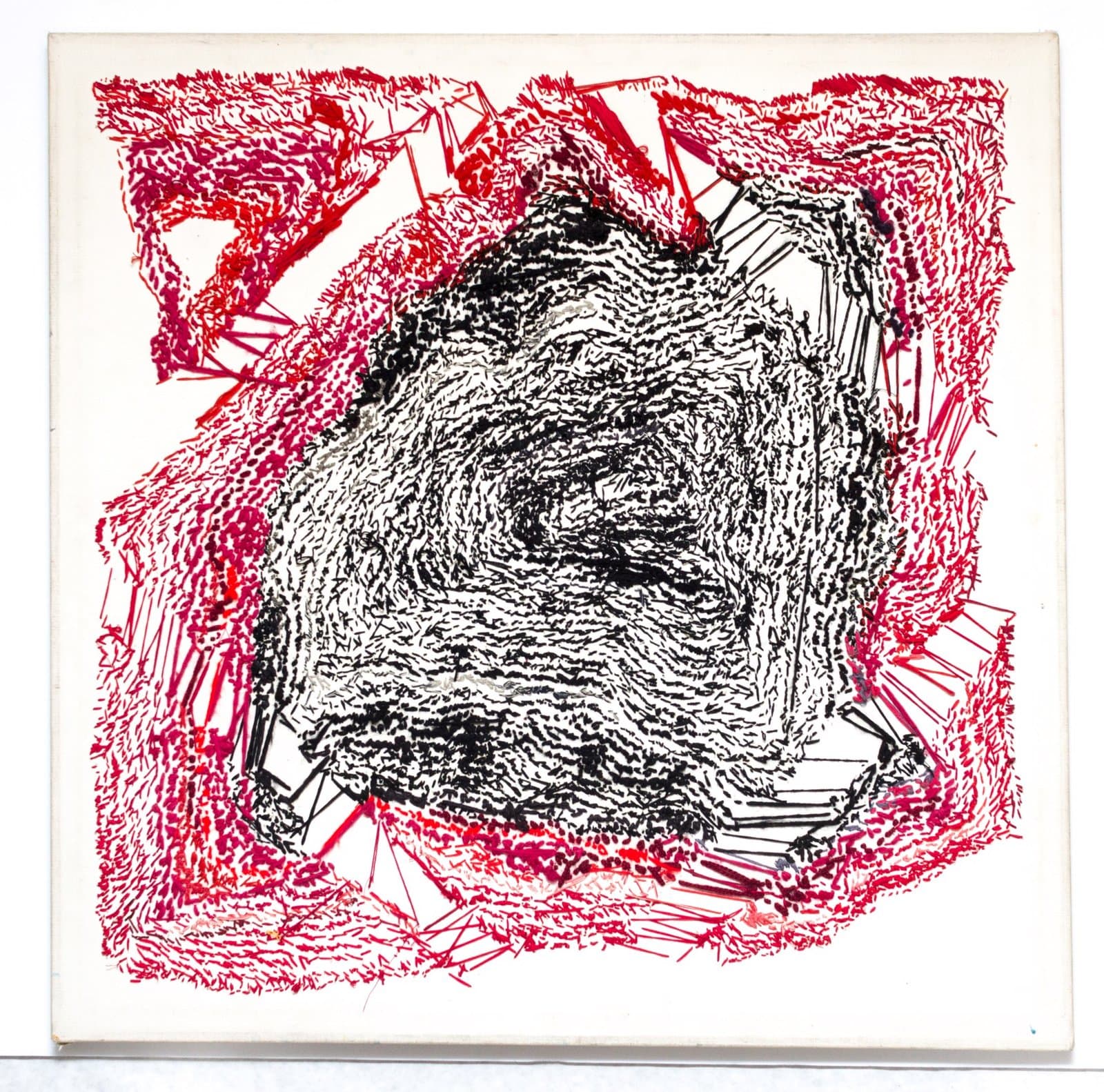 Abstract drawing with densely scribbled black central form surrounded by energetic red and pink marks on white paper