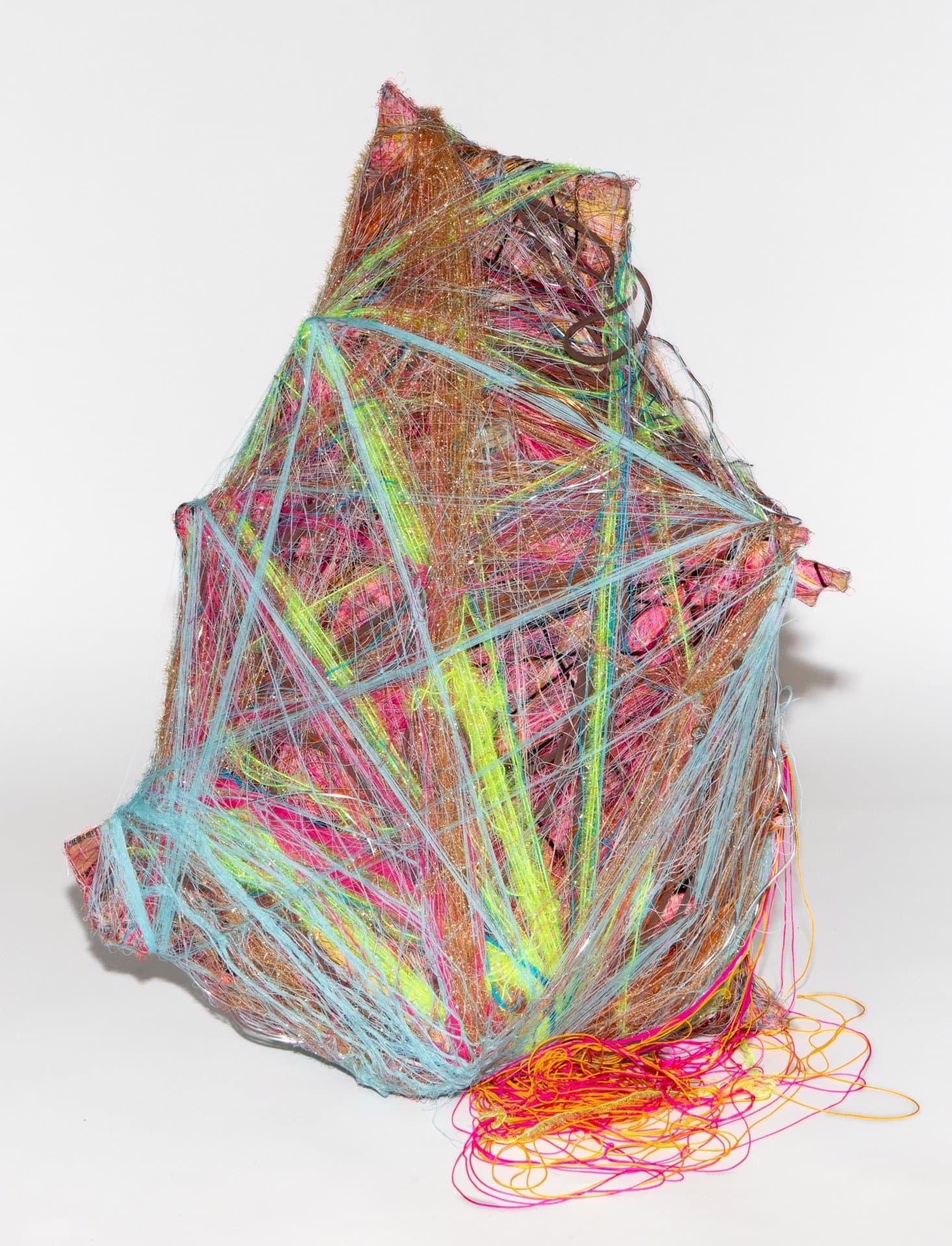 Wrapped sculpture with dense multicolored yarn and thread in bright blues, greens, pinks, and yellows on white background.