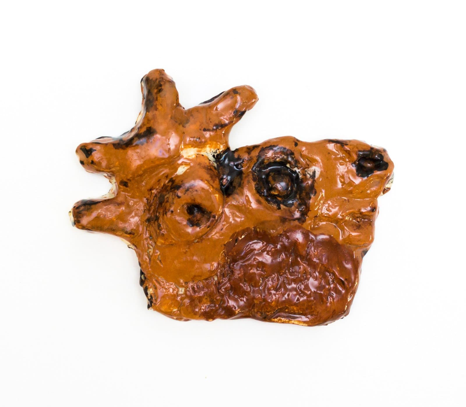 Small glazed ceramic wall sculpture with an irregular organic form in amber brown with dark swirling recesses on white background.