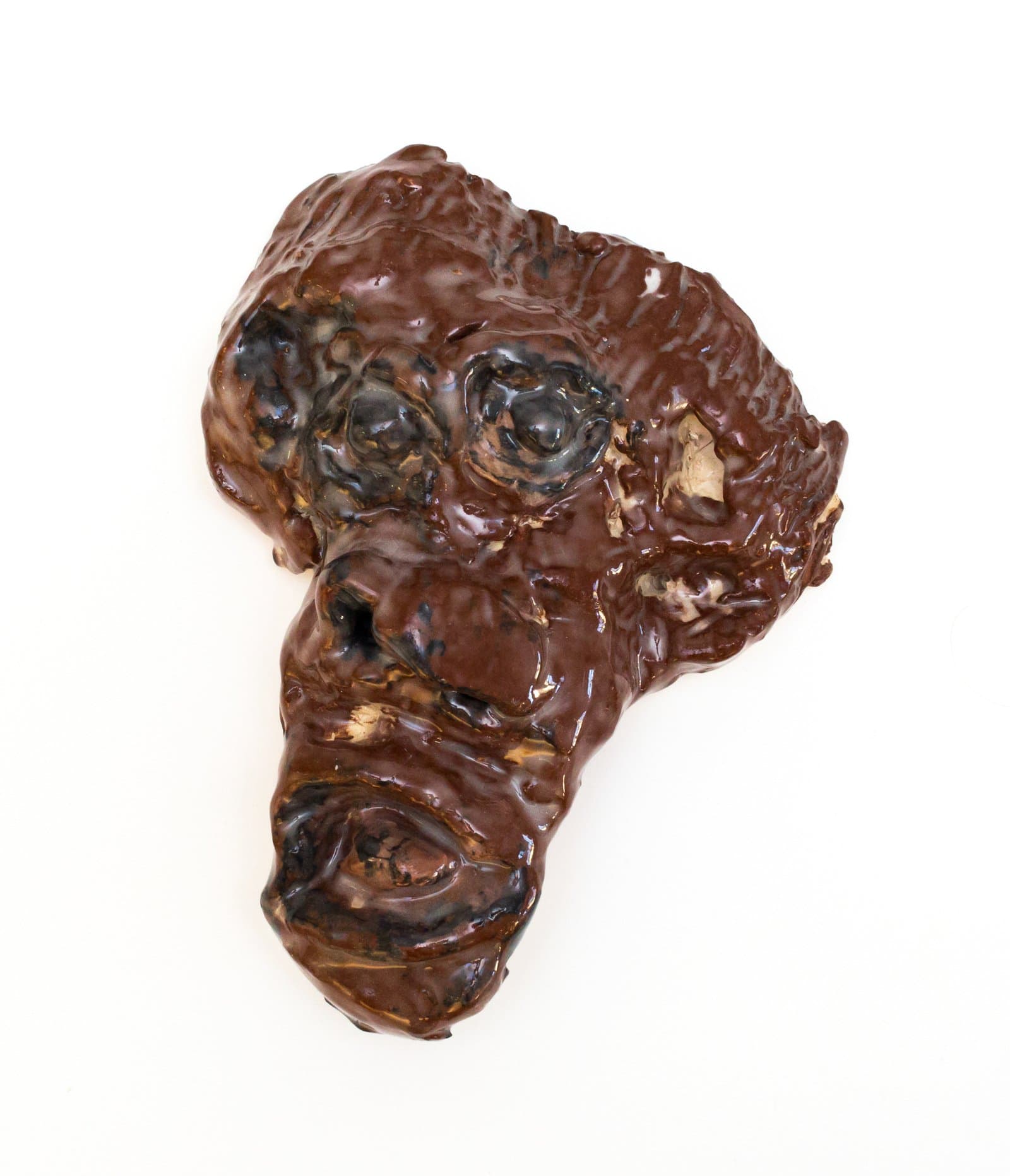 Glazed ceramic face sculpture in deep brown and black tones with heavily textured, irregular surface features.