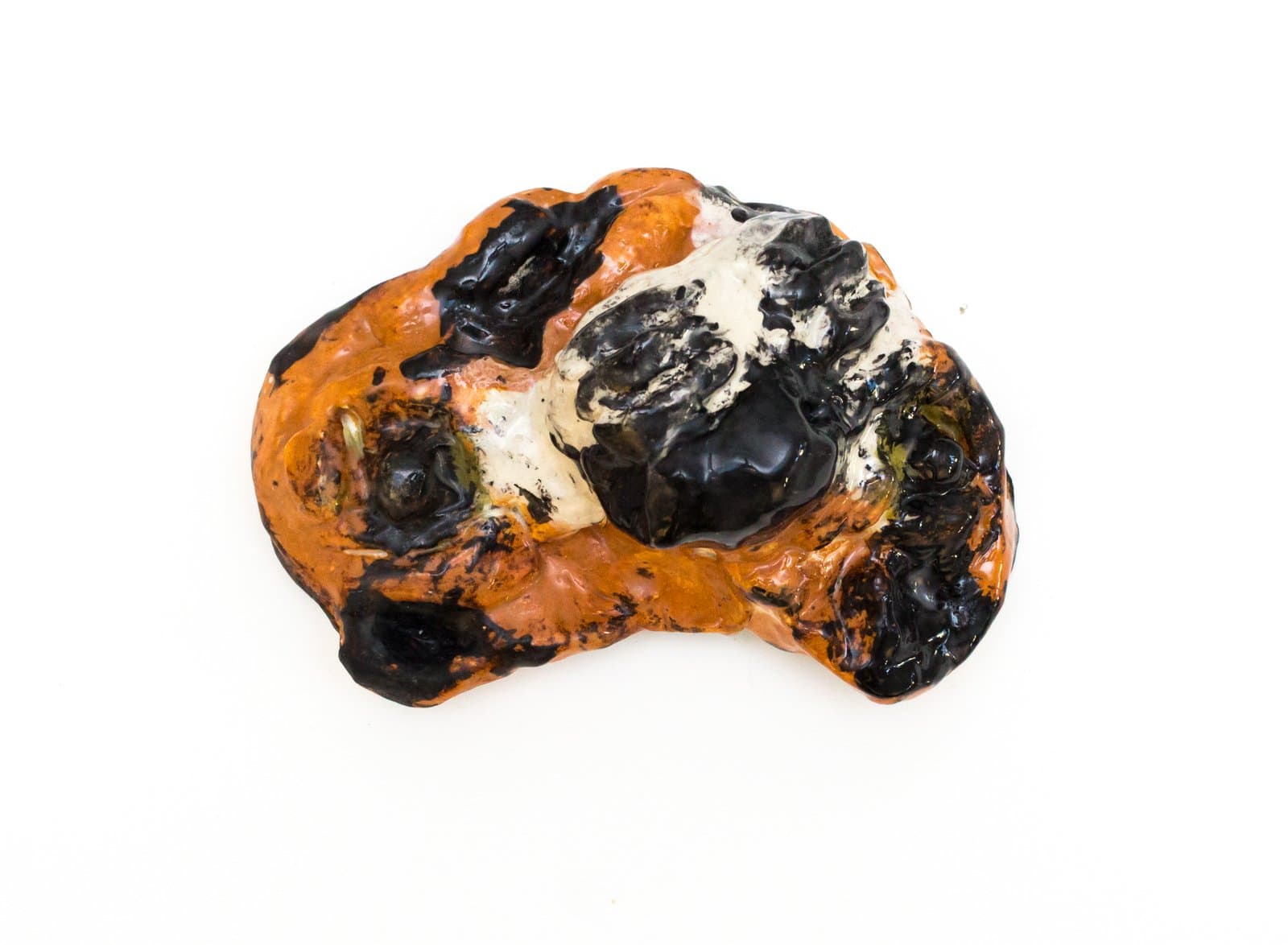 Small ceramic sculpture with an irregular organic form, glazed in orange, black, and white on a white background.