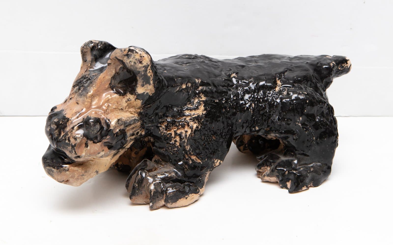Ceramic sculpture of a crouching bear-like animal with glossy black glaze over tan earthenware clay.