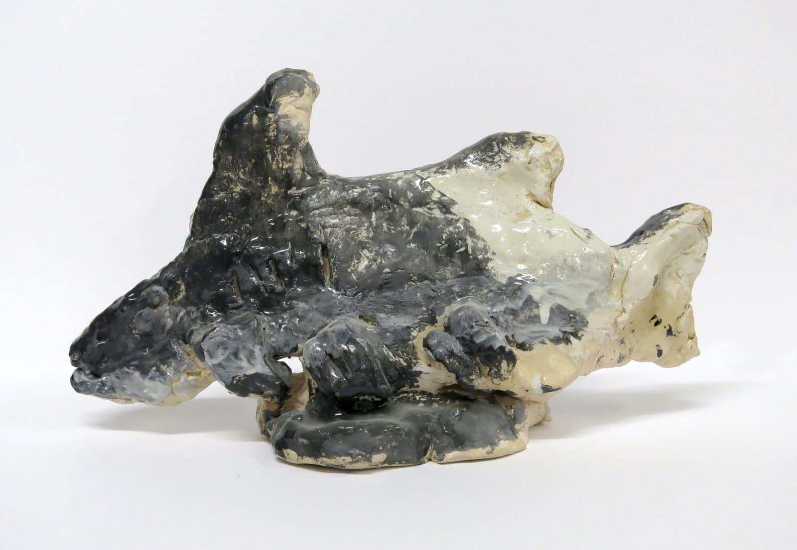 Ceramic sculpture with an irregular, organic form in dark gray and cream glazes, suggesting a landscape or animal shape.
