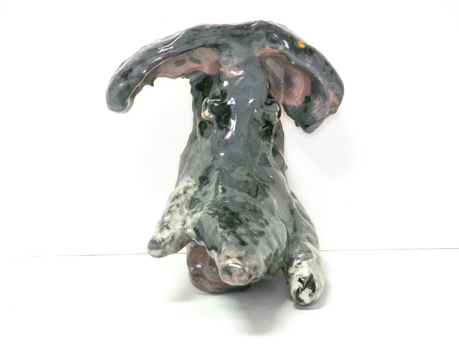 Ceramic sculpture of a reclining dog, glazed in dark gray with pink inner ears and white speckled paws.