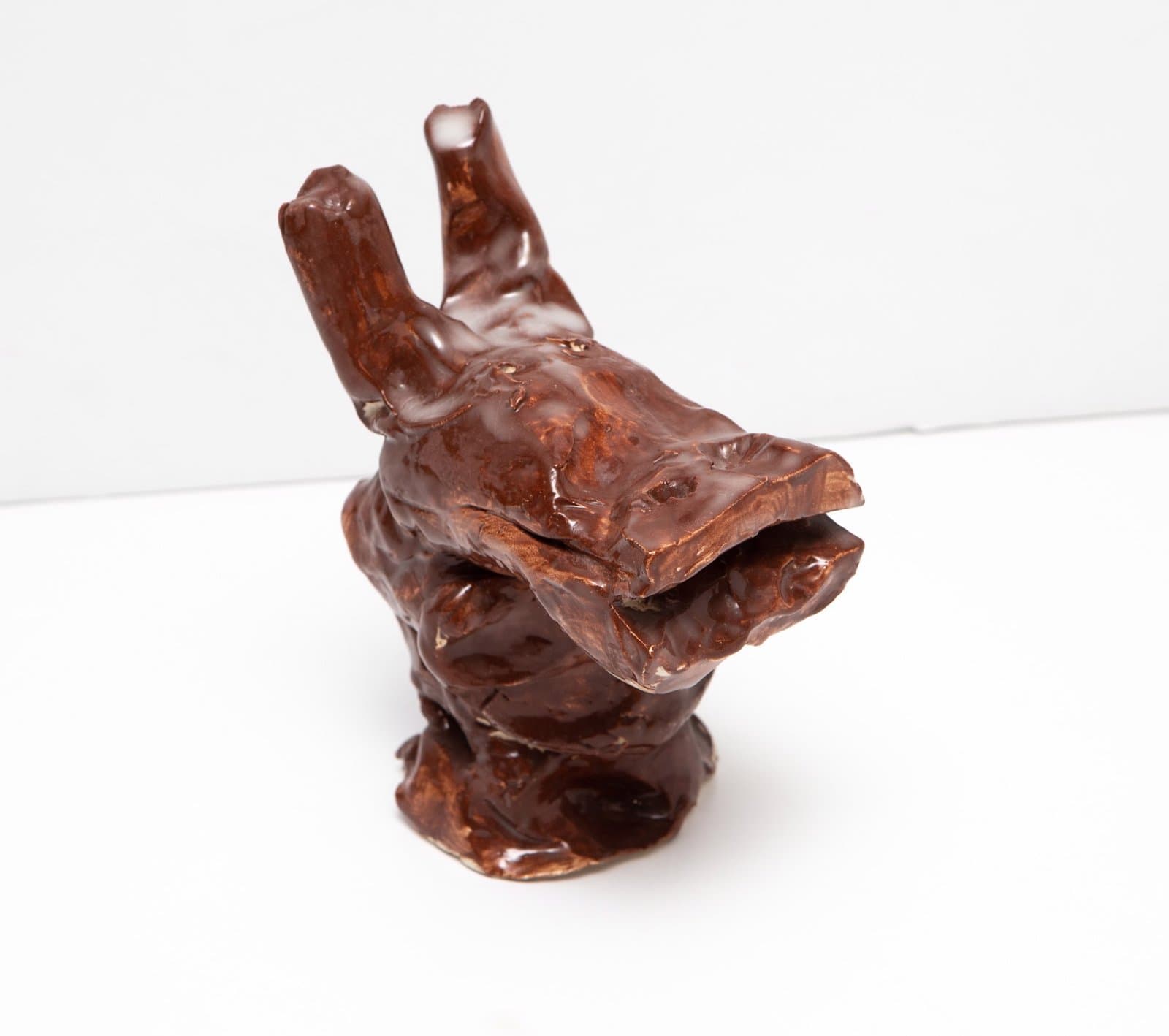 Ceramic sculpture of brown glazed hand with fingers pointing upward on white background.