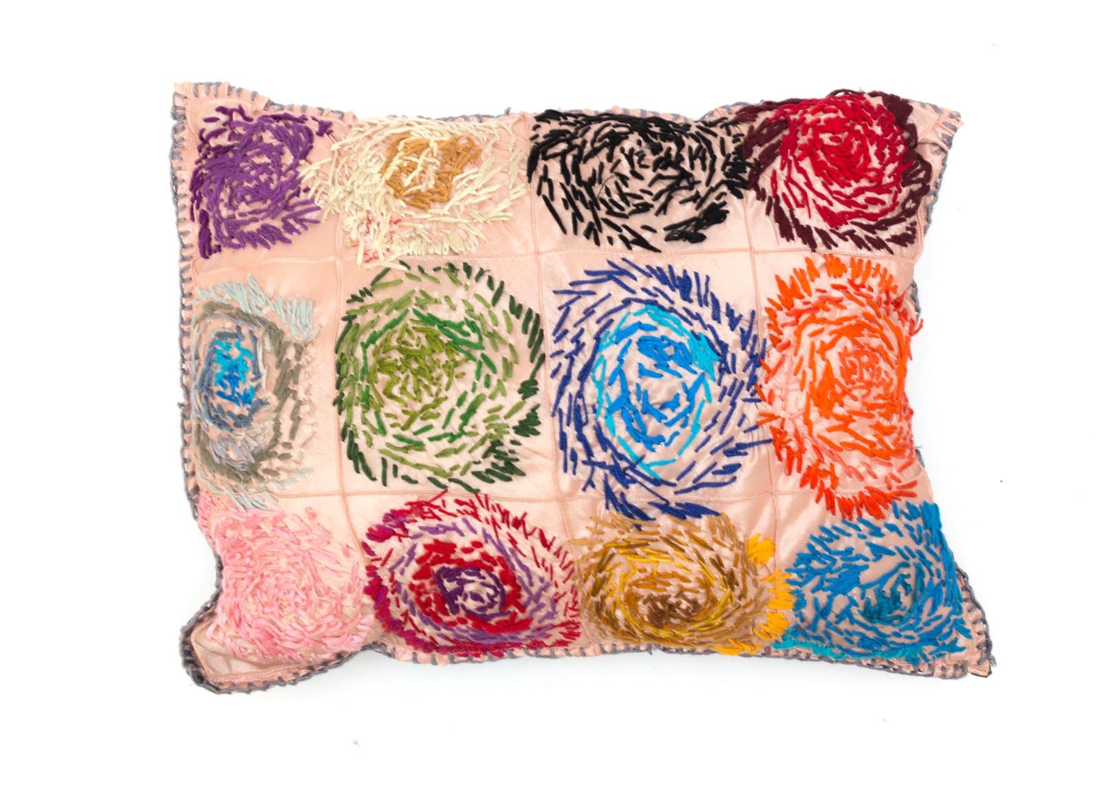 Embroidered pillow on pink fabric featuring a grid of multicolored spiral rosette motifs in thread.
