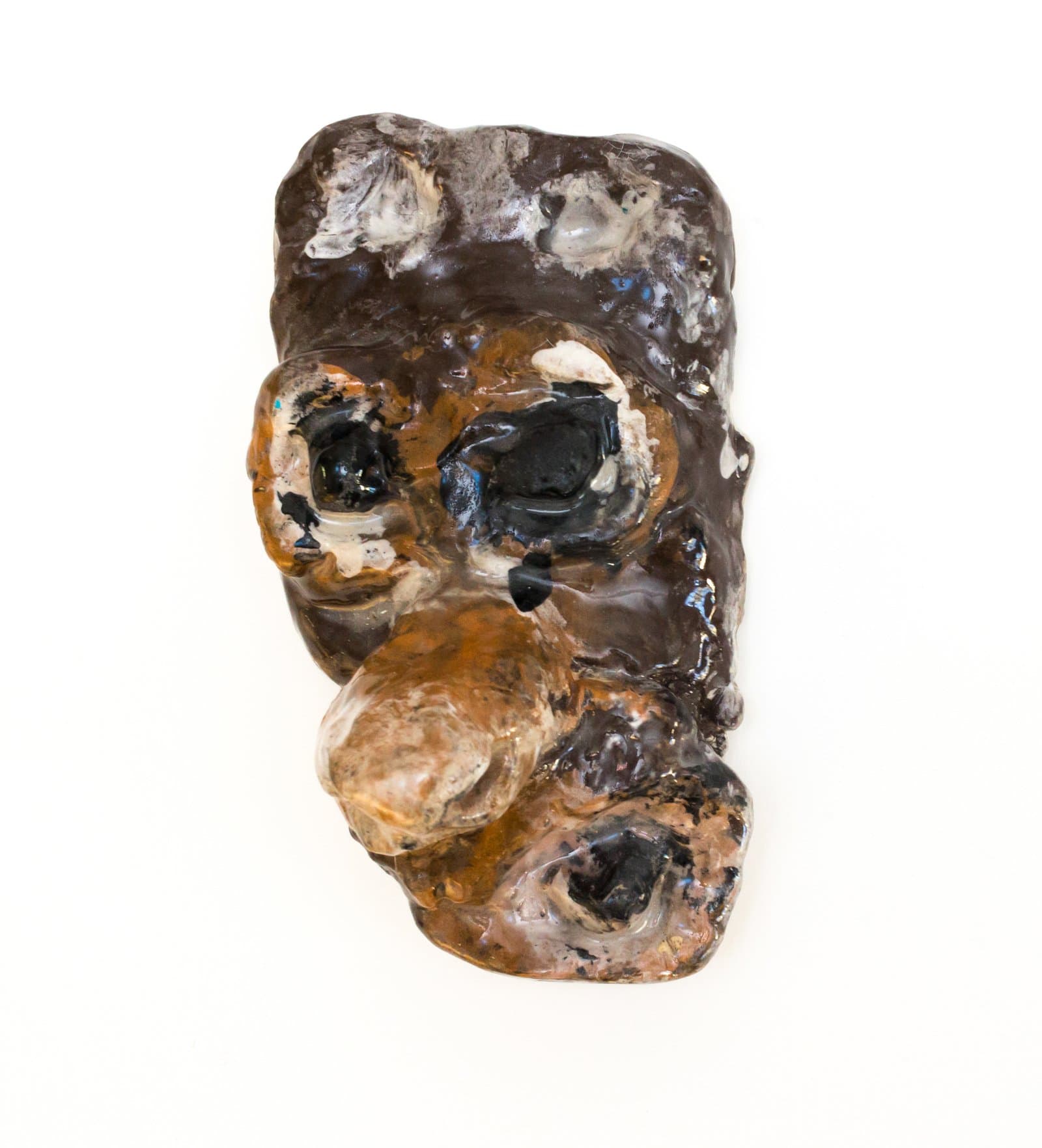 Small ceramic face mask sculpture with heavily textured glazed surface in dark brown, amber, and black tones.