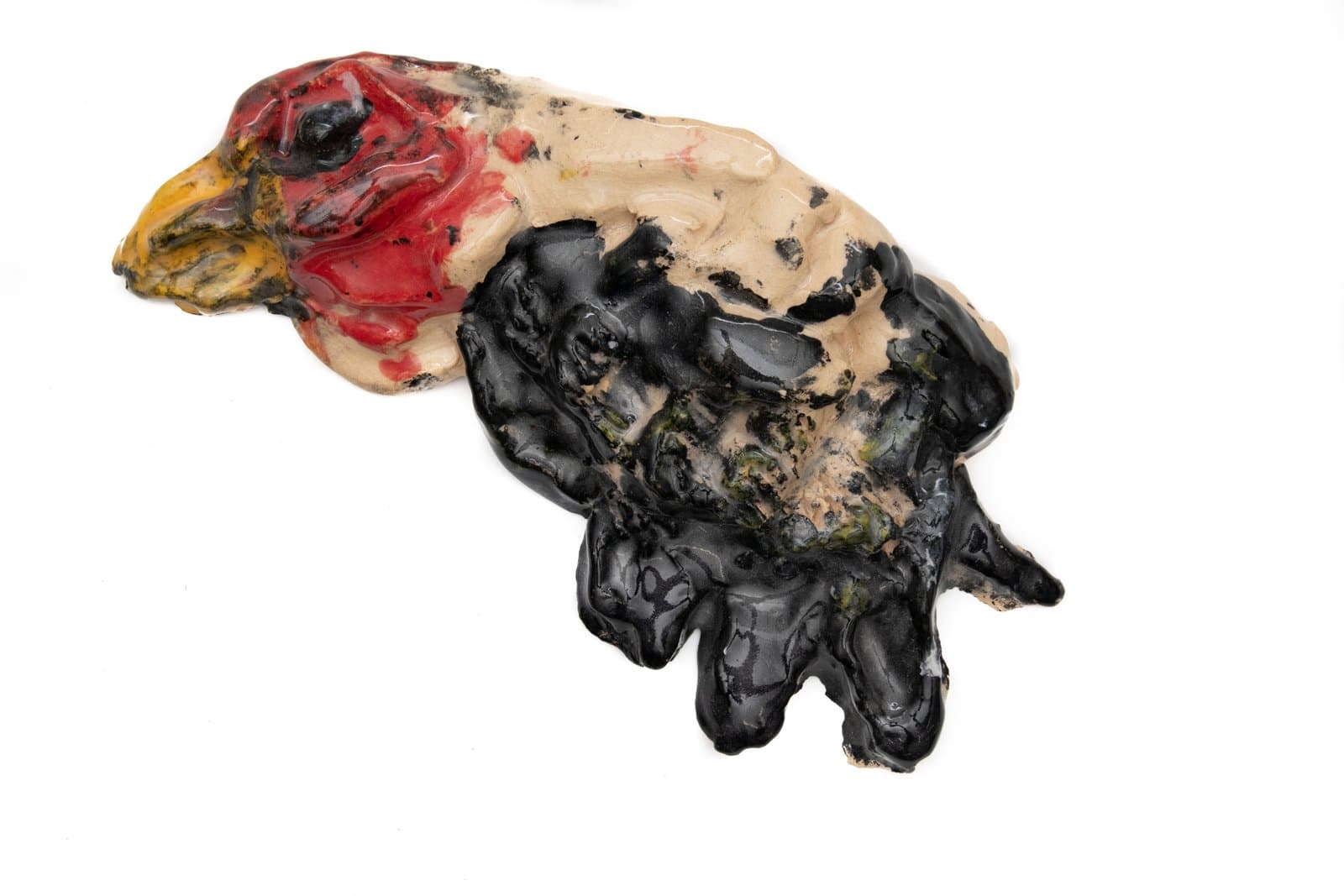 Ceramic wall sculpture of a bird with a red and yellow head and black textured body on white background.