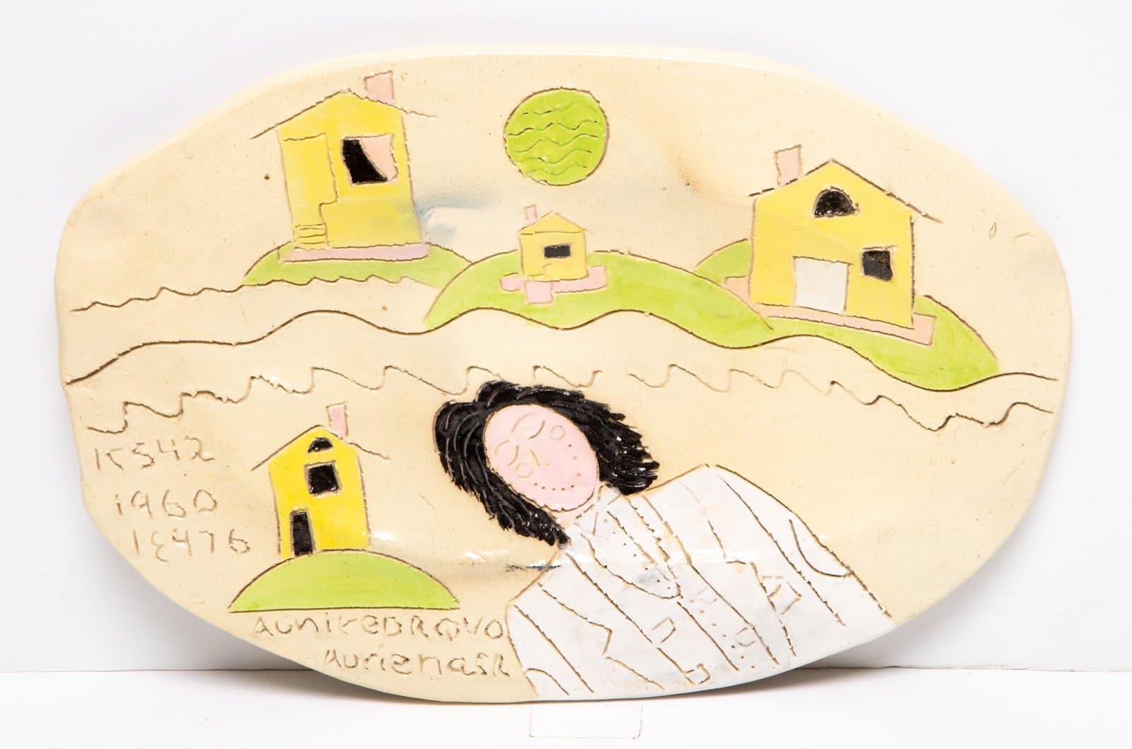 Oval ceramic platter with painted figure, yellow houses, and green hills in earth tones with handwritten text