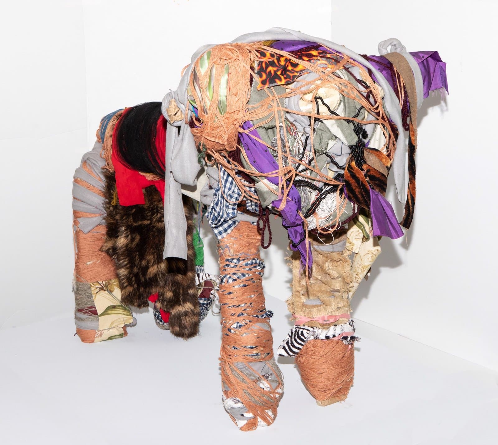 Mixed-media elephant sculpture wrapped in colorful fabric strips, ribbons, and fur in purple, orange, and brown tones