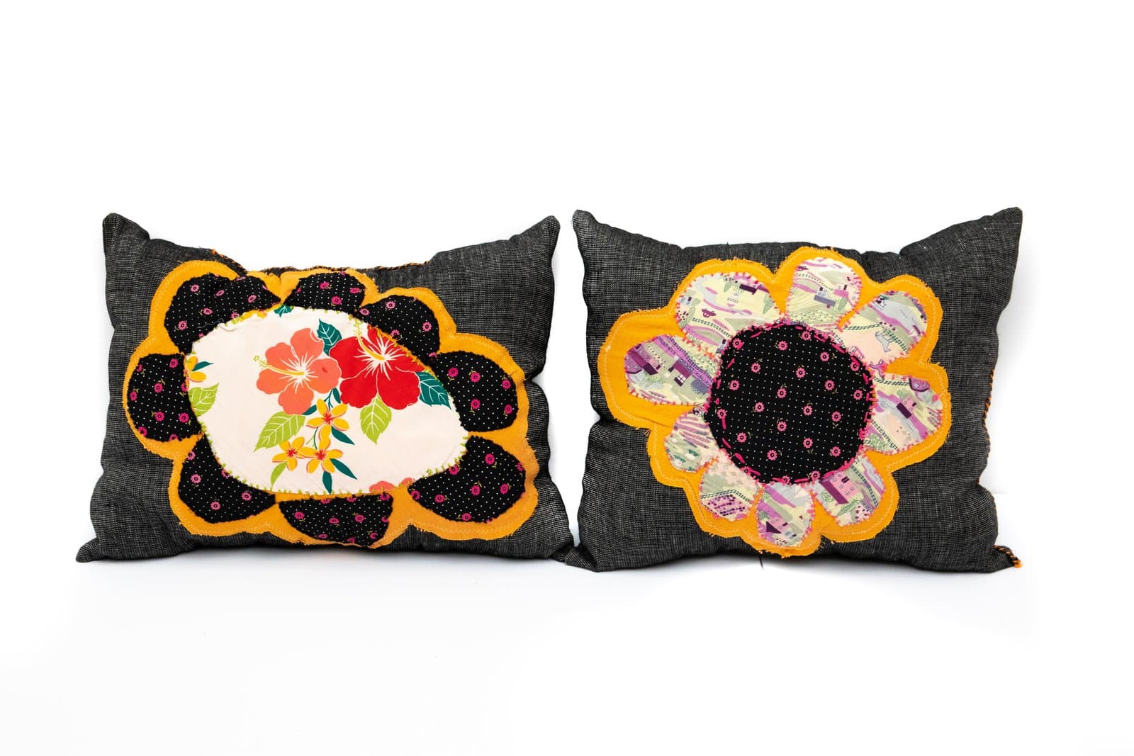 Two dark denim pillows with fabric appliqué flower medallions in black, orange, and multicolor patterned textiles.