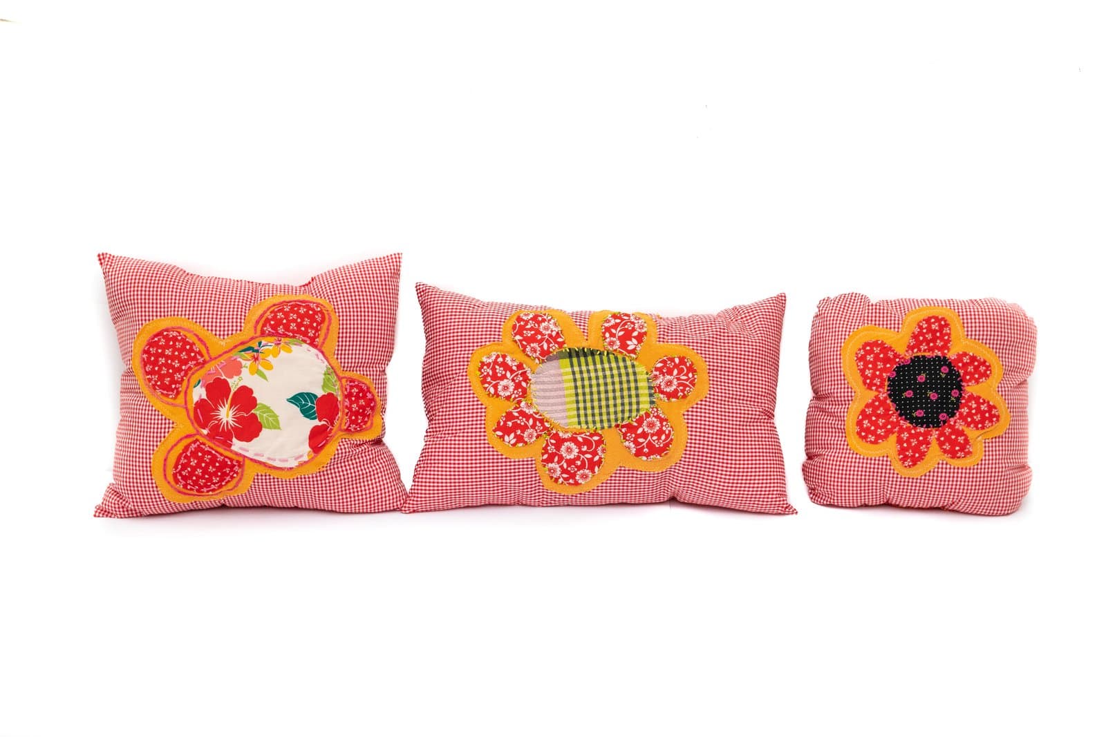 Three red gingham fabric pillows with appliquéd flower and turtle motifs in orange, red, yellow, and green.