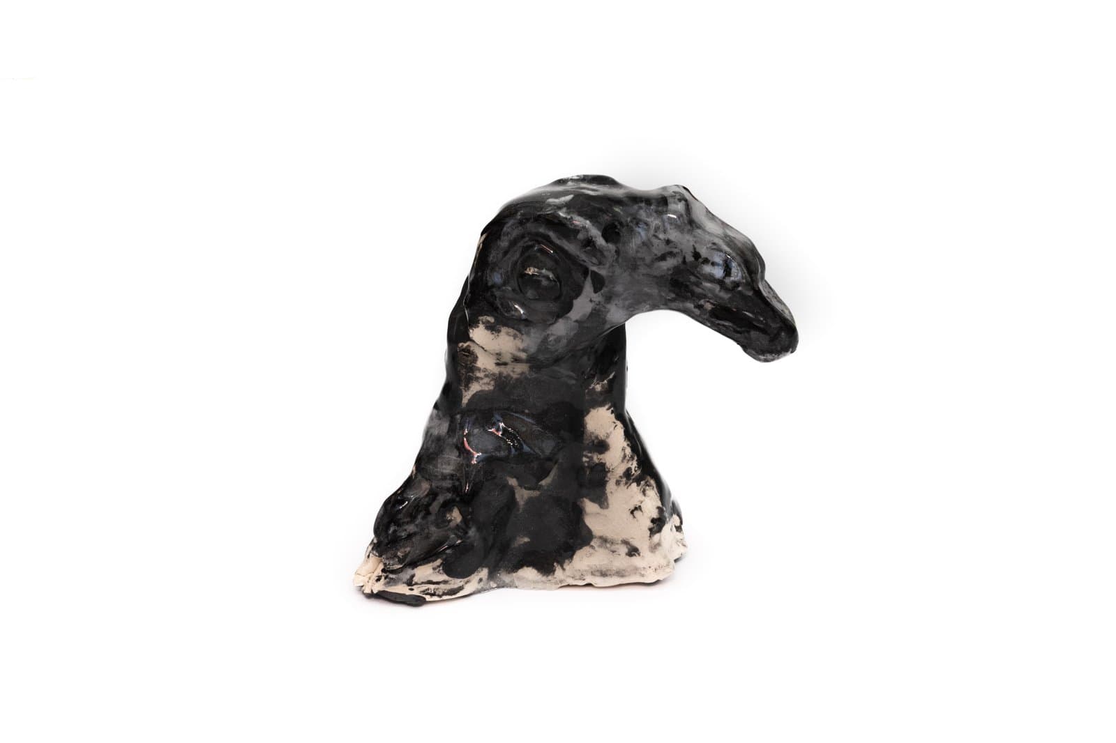 Ceramic sculpture of an animal head, likely a dog or camel, glazed in black and cream tones.