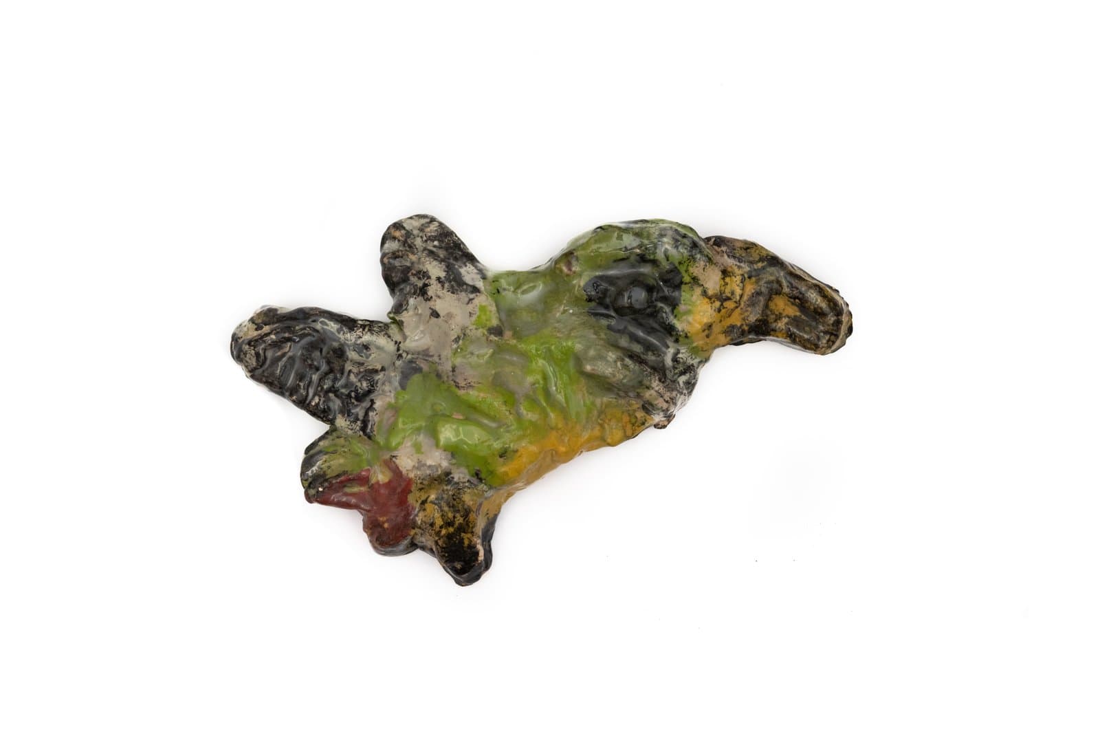Small irregularly shaped ceramic sculpture with a roughly textured surface in black, green, yellow, and red glazes.