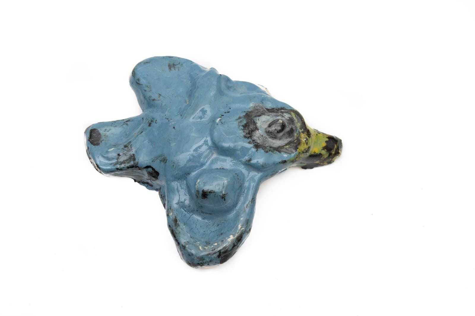 Glazed ceramic sculpture with an irregular, lobed form suggesting an animal face, primarily in matte blue with black and yellow accents.