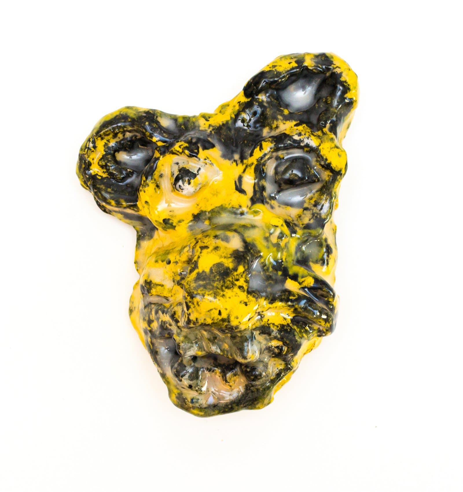 Glazed ceramic wall-mounted face sculpture with animal-like features in mottled yellow and black glaze.