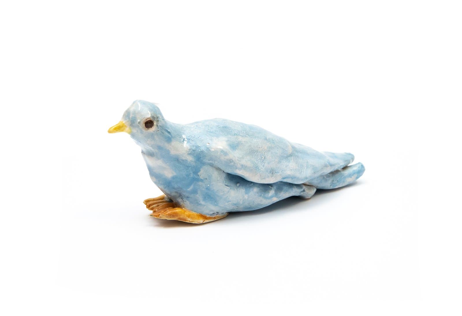 Small ceramic sculpture of a resting bird glazed in mottled blue with a yellow beak and orange-yellow feet.