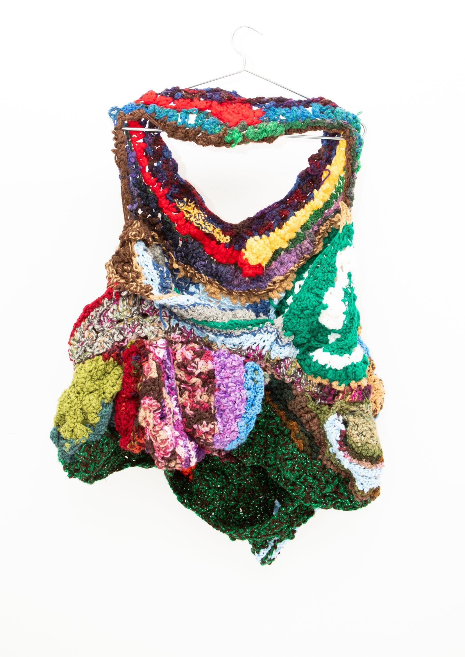 Crocheted textile sculpture hung on a wire hanger, featuring densely layered multicolor yarn in irregular, bulging forms.