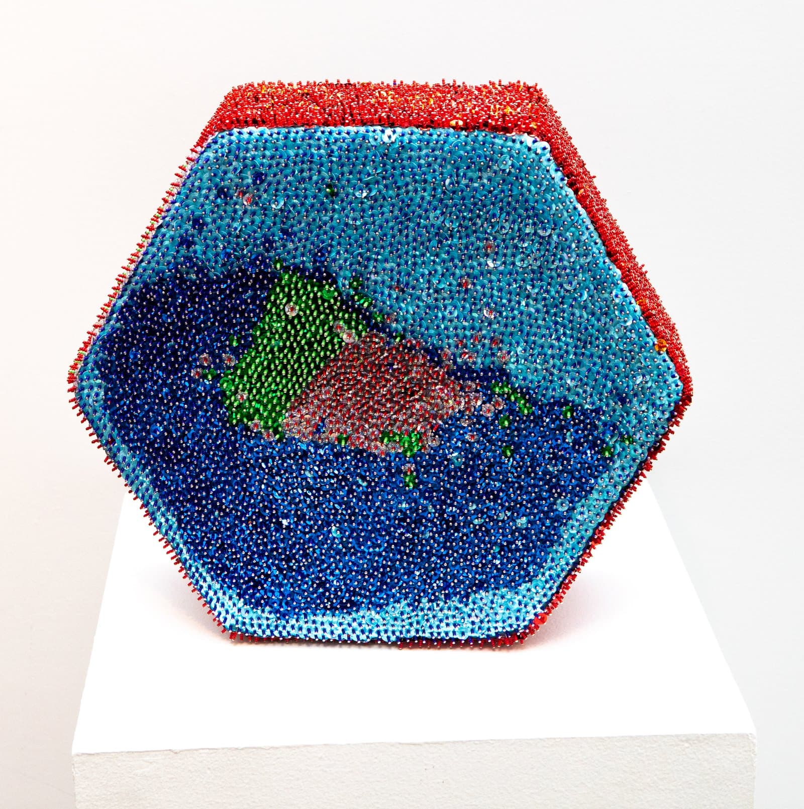 Hexagonal mixed media sculpture densely covered in beads, featuring blue interior with green and red forms, red beaded edges.