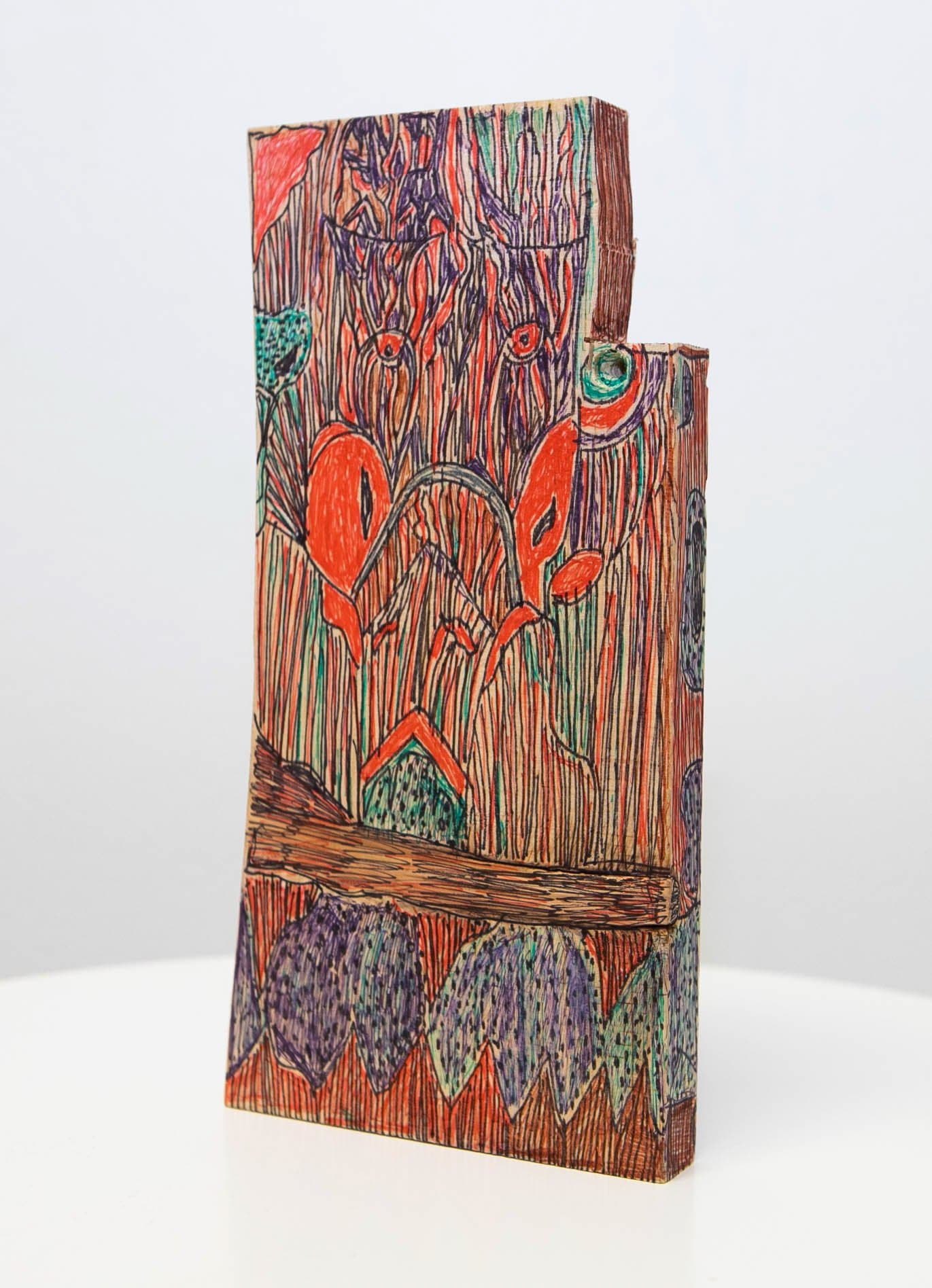 Pen on wood sculpture, a stepped rectangular block densely covered in red, purple, green, and orange organic forms and vertical lines.