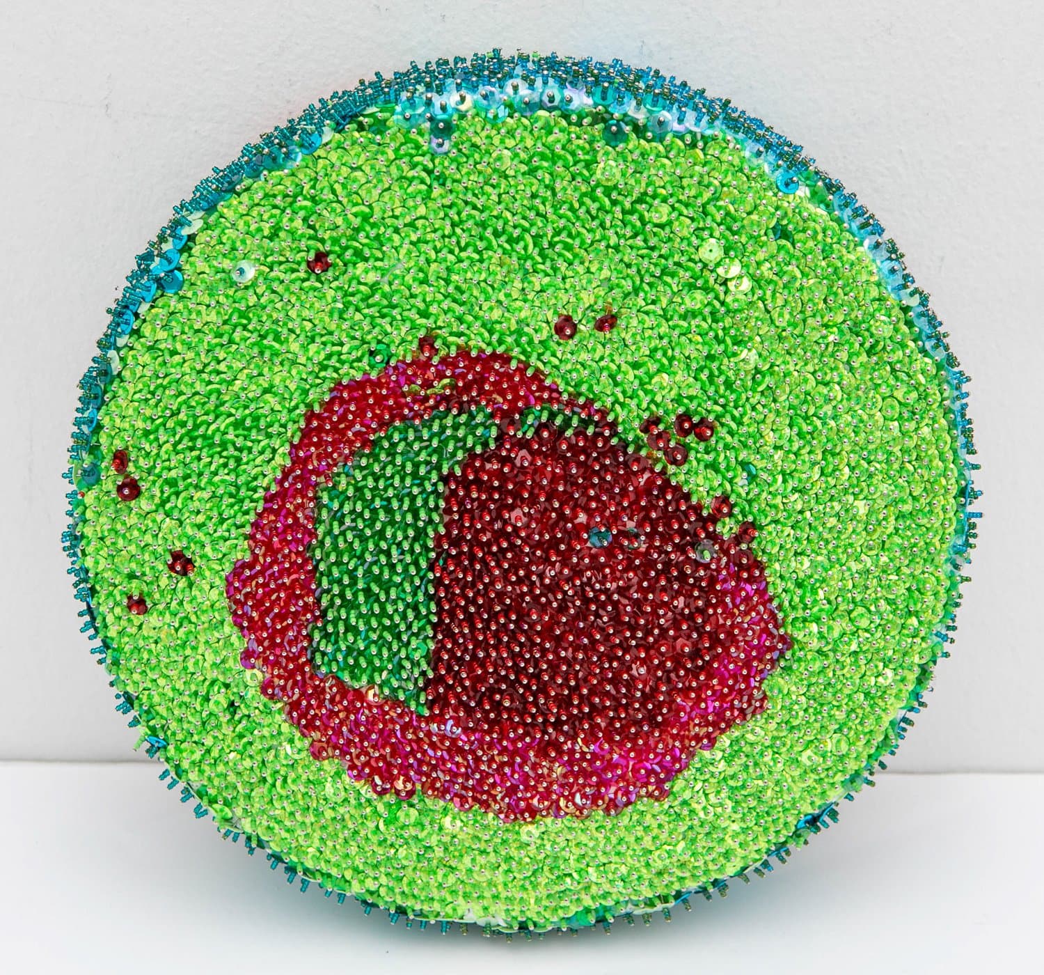 Circular sculptural form densely covered in bright green sequins and beads with a central red and magenta beaded oval motif.