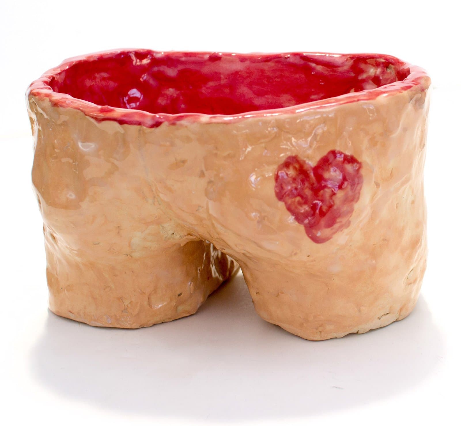Ceramic sculpture resembling human buttocks with heart motif, glazed in flesh tones with red interior