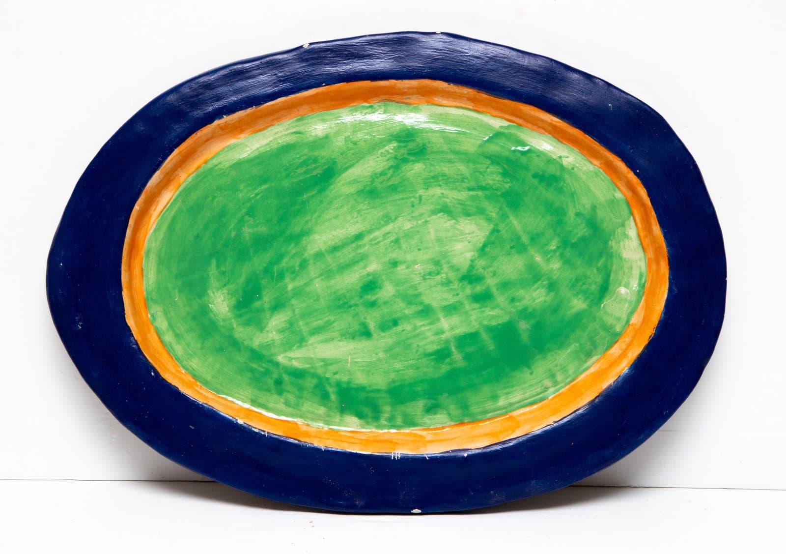 Oval ceramic bowl with concentric bands of deep blue rim, orange middle ring, and bright green center interior.