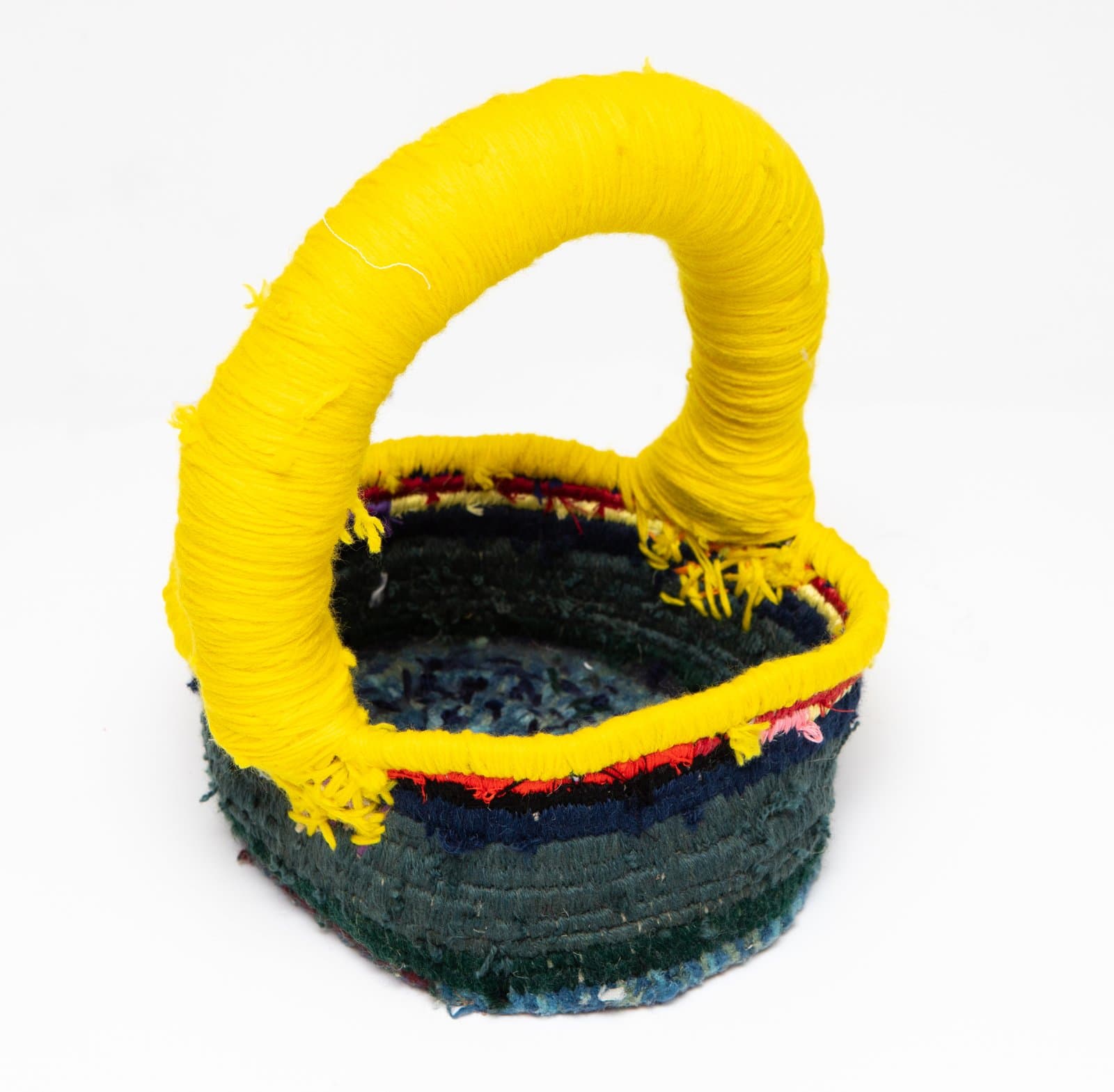 Small coiled textile basket with dark teal body and a bold yellow yarn-wrapped arched handle, on white background.
