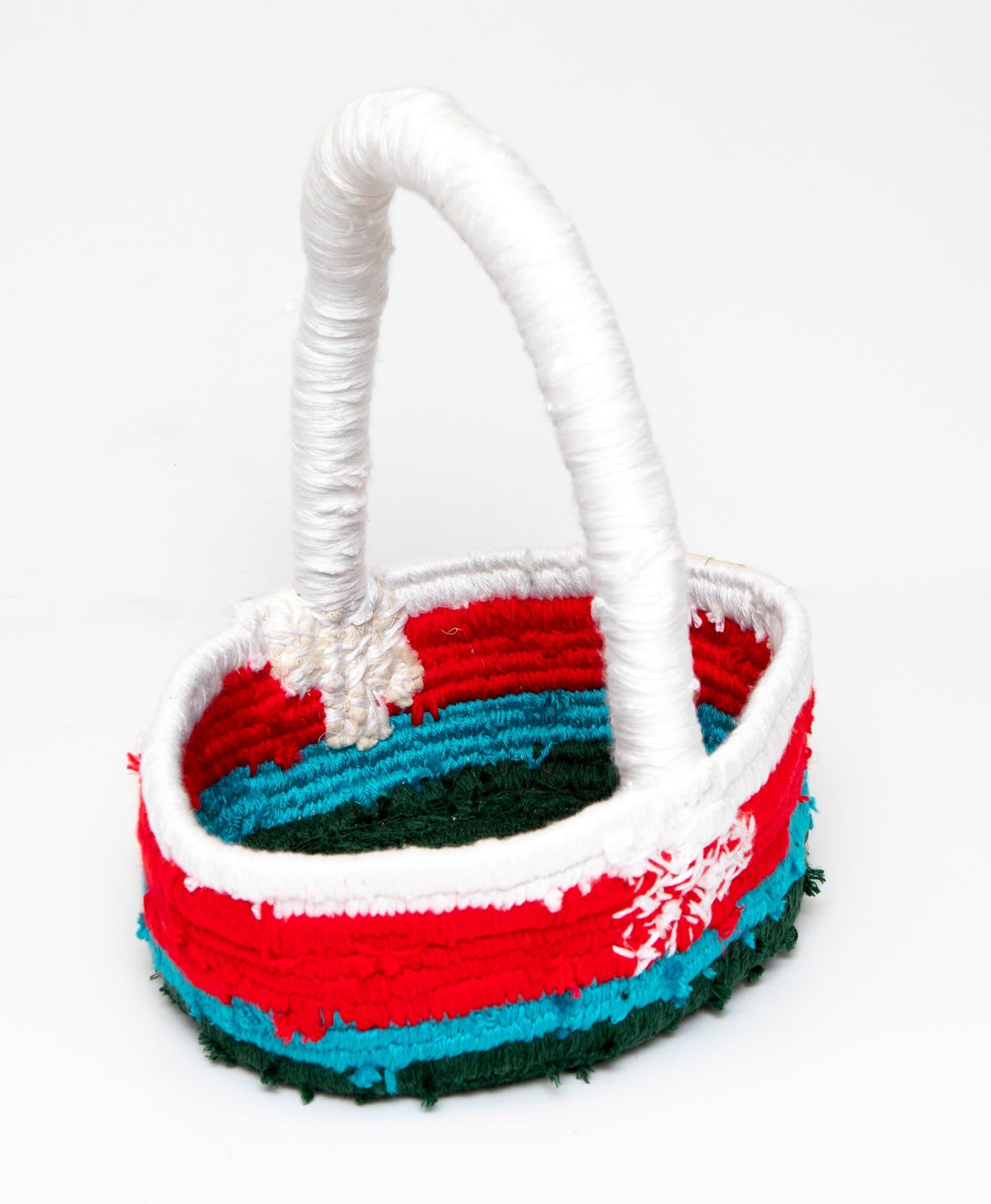 Small handmade textile basket with arched handle, wrapped in red, teal, dark green, and white yarn.