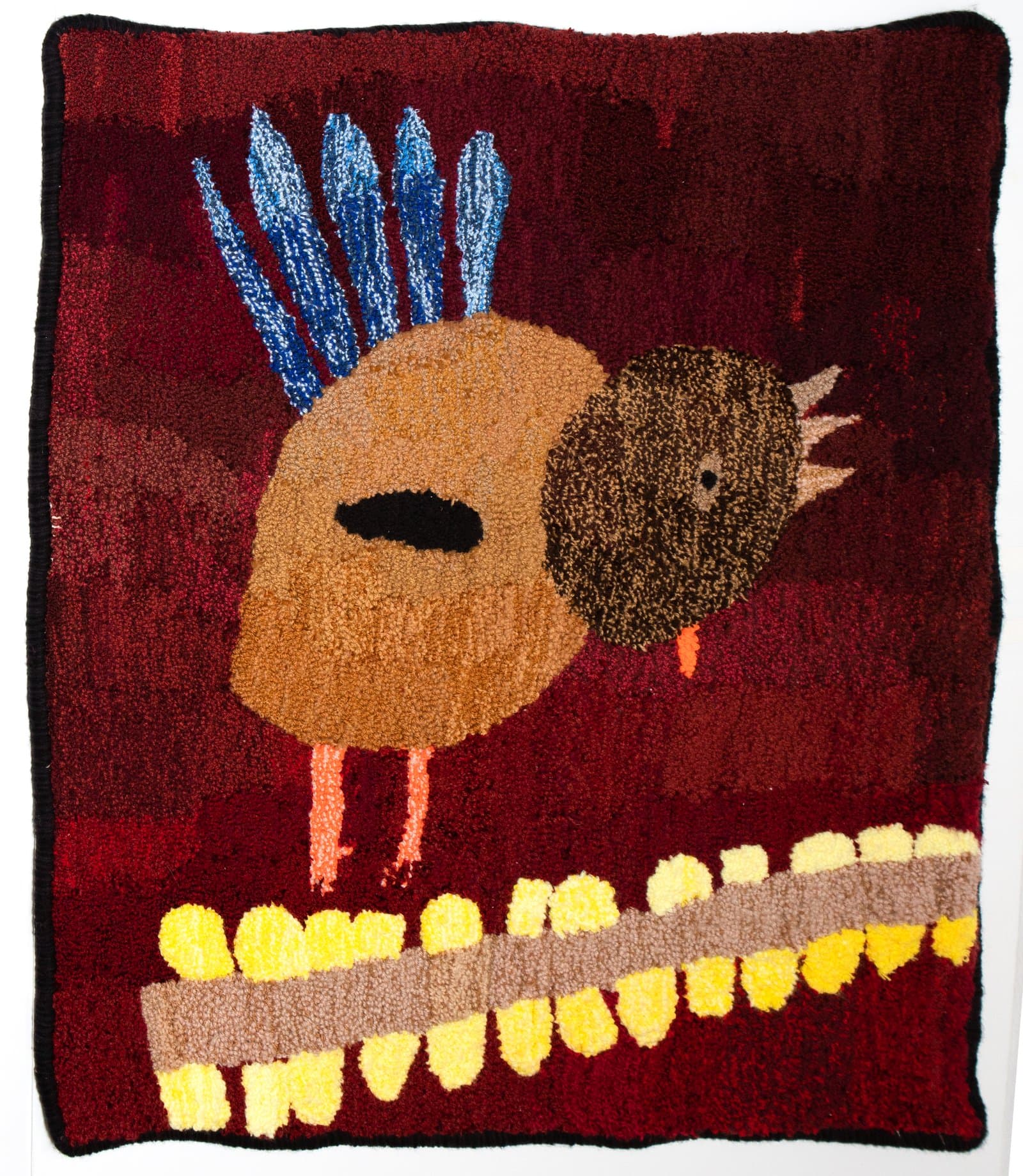 Tufted rug depicting two round birds on a dark red background, with blue feathers, orange legs, and yellow border detail.