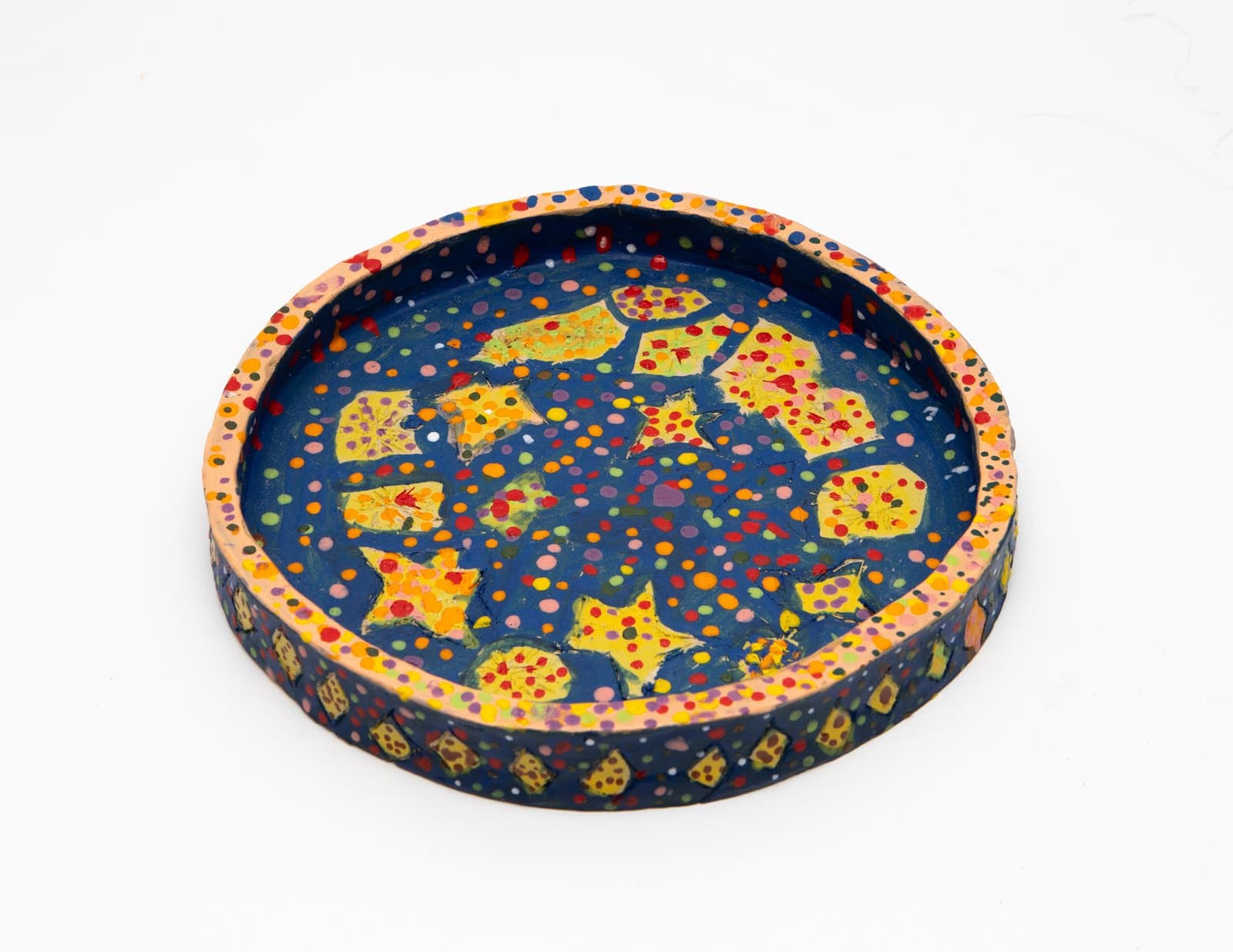 Round ceramic tray with deep blue interior decorated with yellow star and leaf shapes amid multicolored polka dots, peach rim.