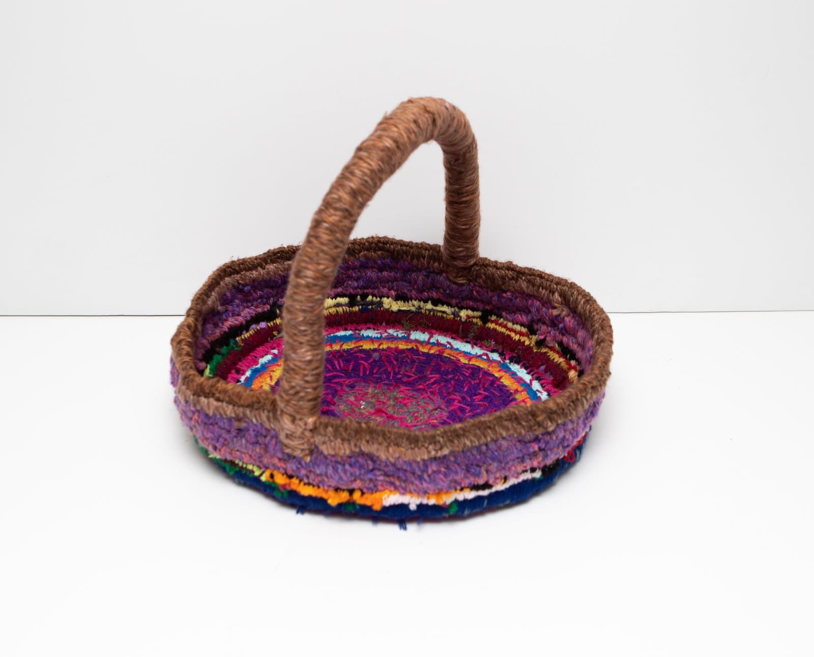 Oval woven basket with arched handle, constructed from multicolored fabric strips and brown yarn, approximately 13x16 inches.
