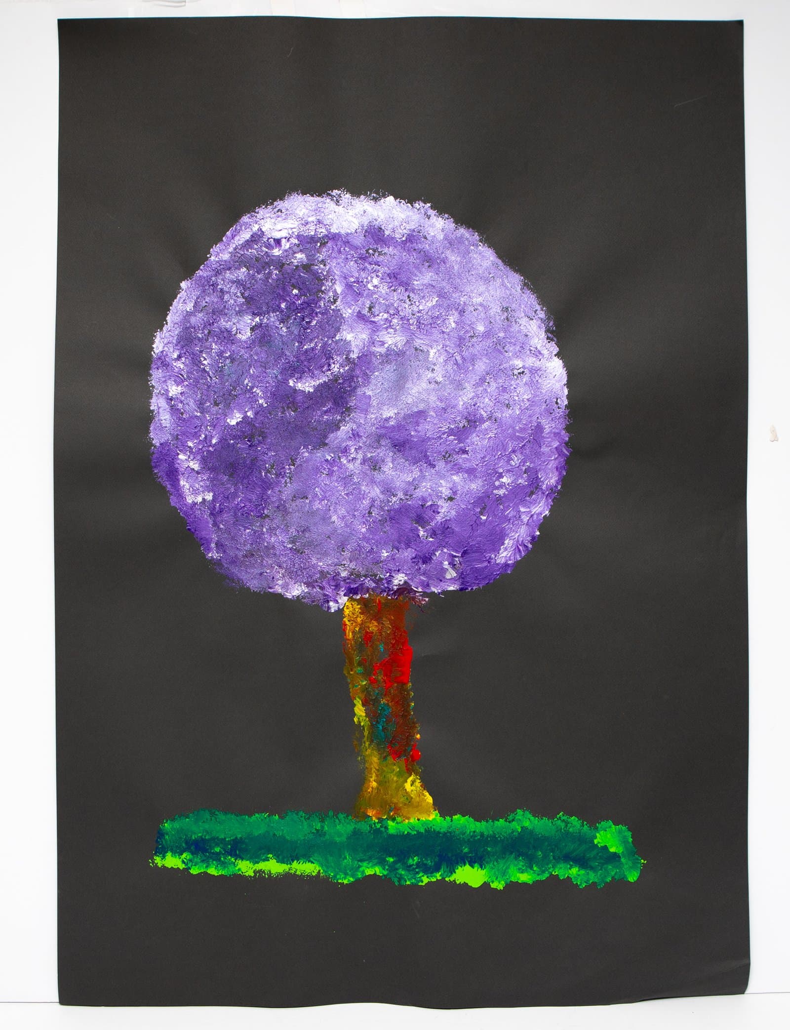 Acrylic painting of a tree with a large round purple canopy, multicolored trunk, and green ground strip on black paper.
