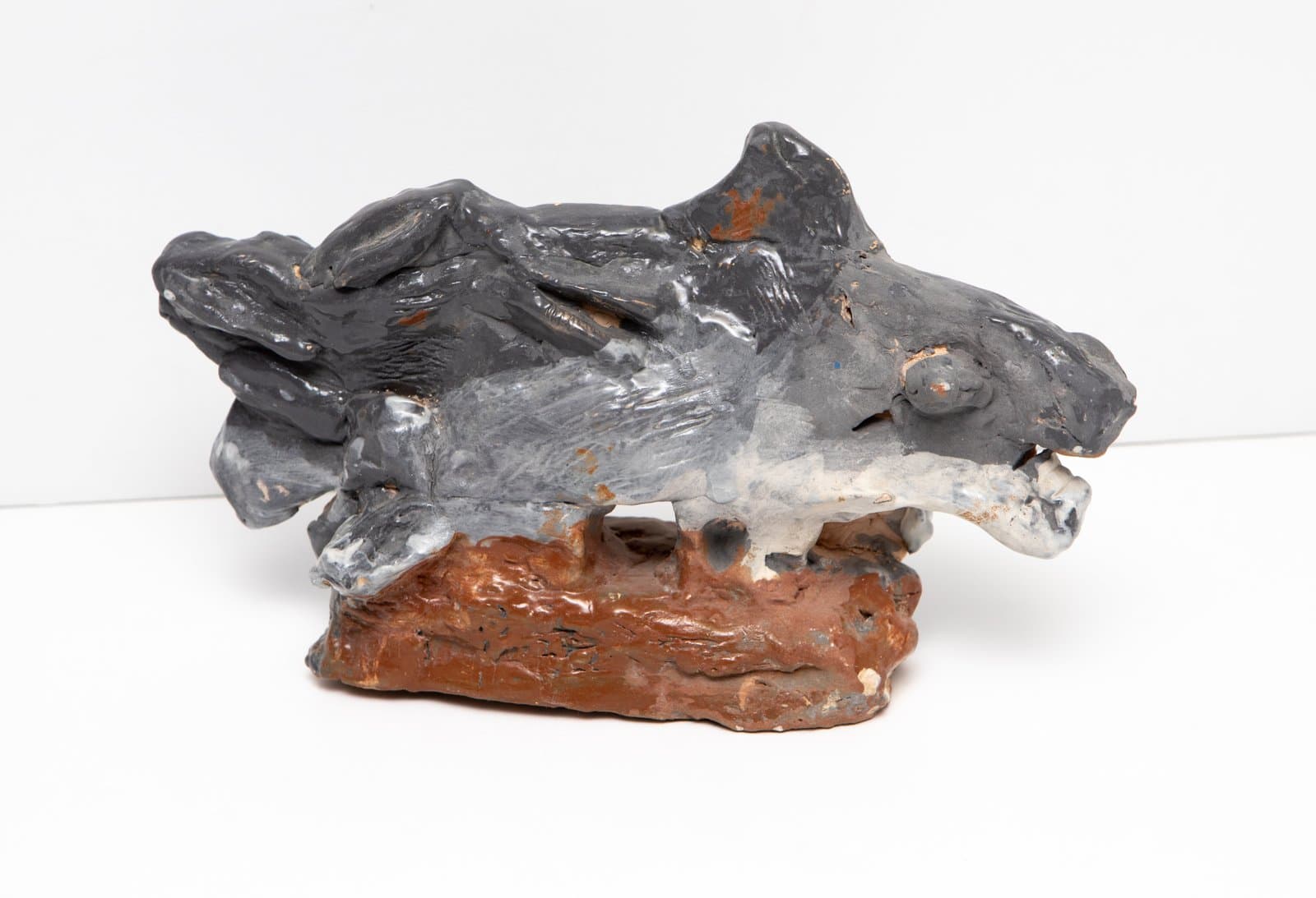 Ceramic sculpture of an animal figure in dark gray glaze on a rust-brown base, with rough hand-built texture.