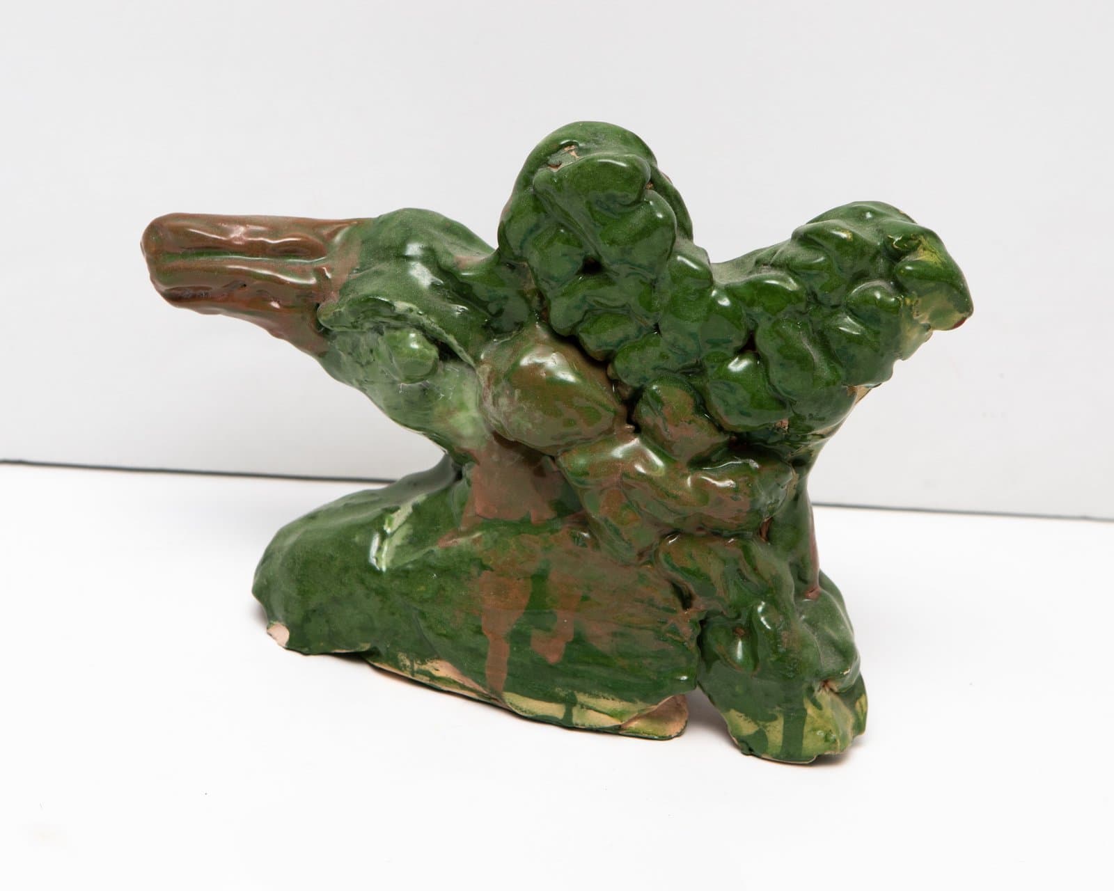 Ceramic sculpture of a bird figure glazed in mottled green and brown, with textured, lumpy surface forms.