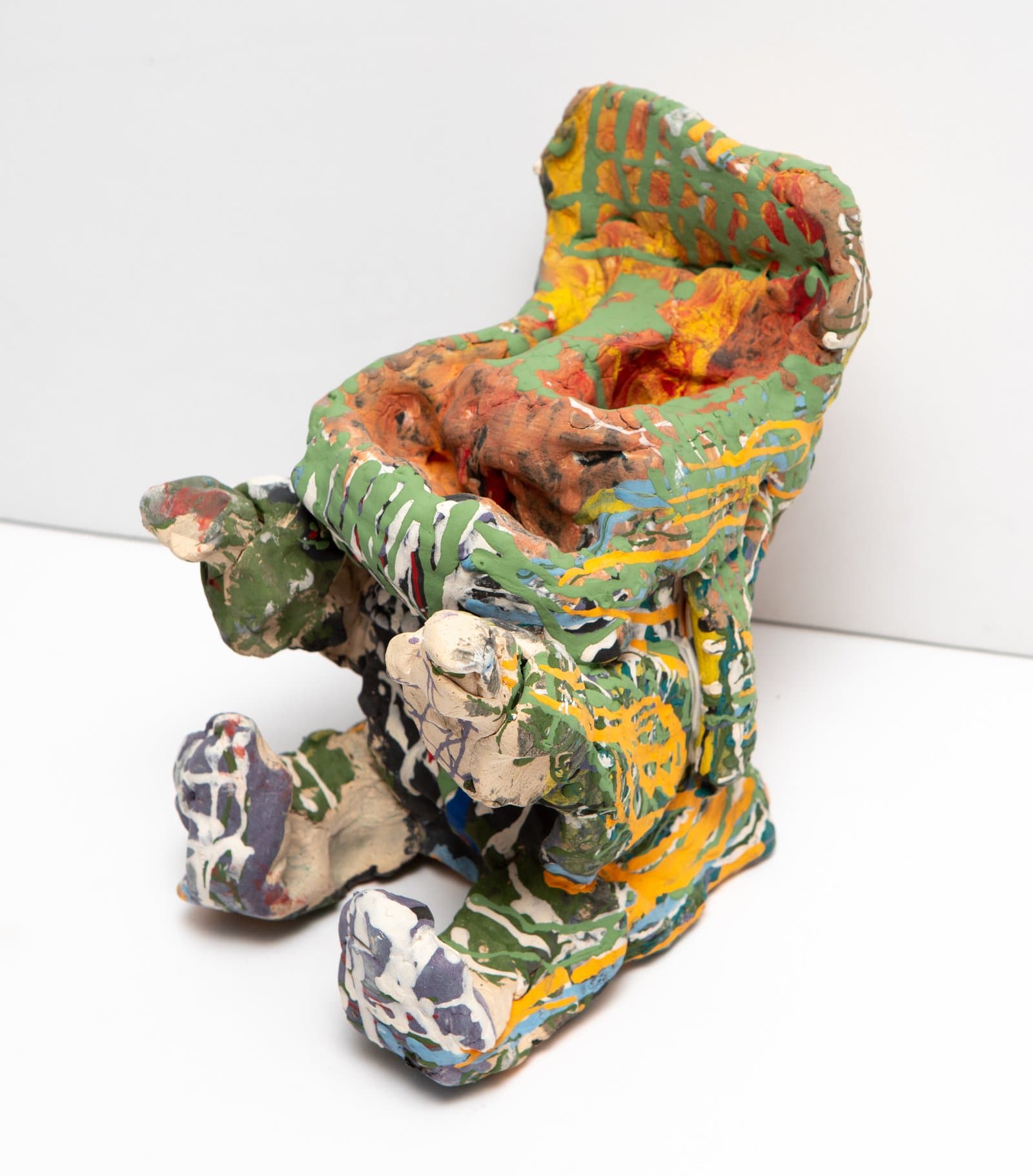 Ceramic sculpture with an open top, densely painted in green, yellow, orange, blue, and white on an irregular figurative form.