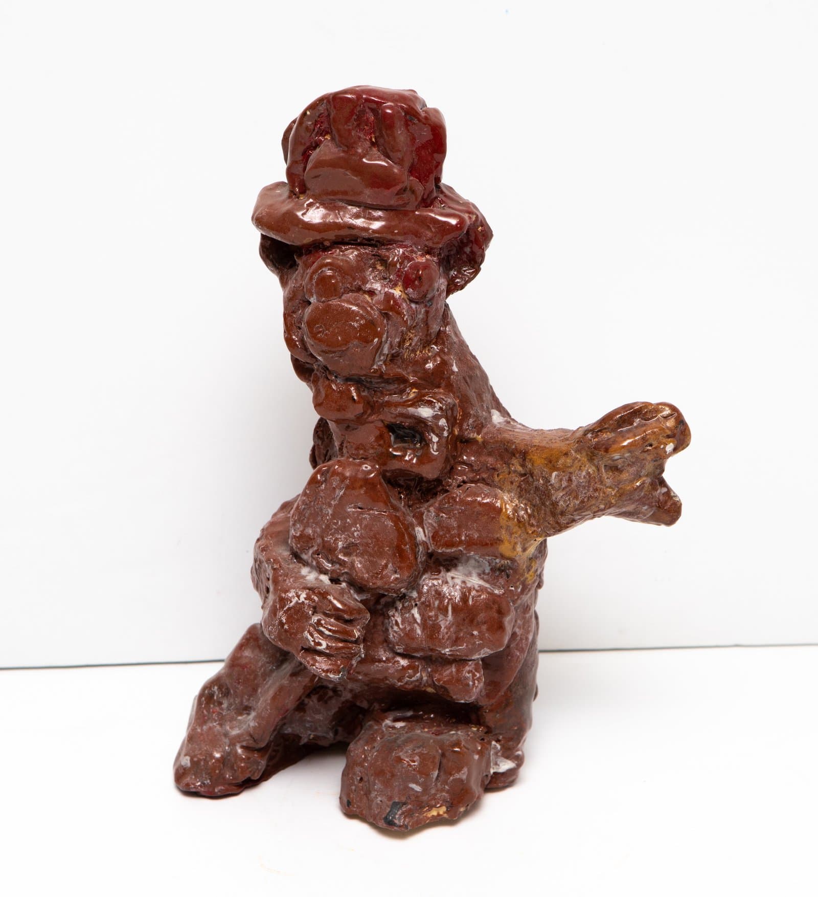 Ceramic sculpture of a rough, lumpy humanoid figure with a hat, covered in dark reddish-brown glaze.