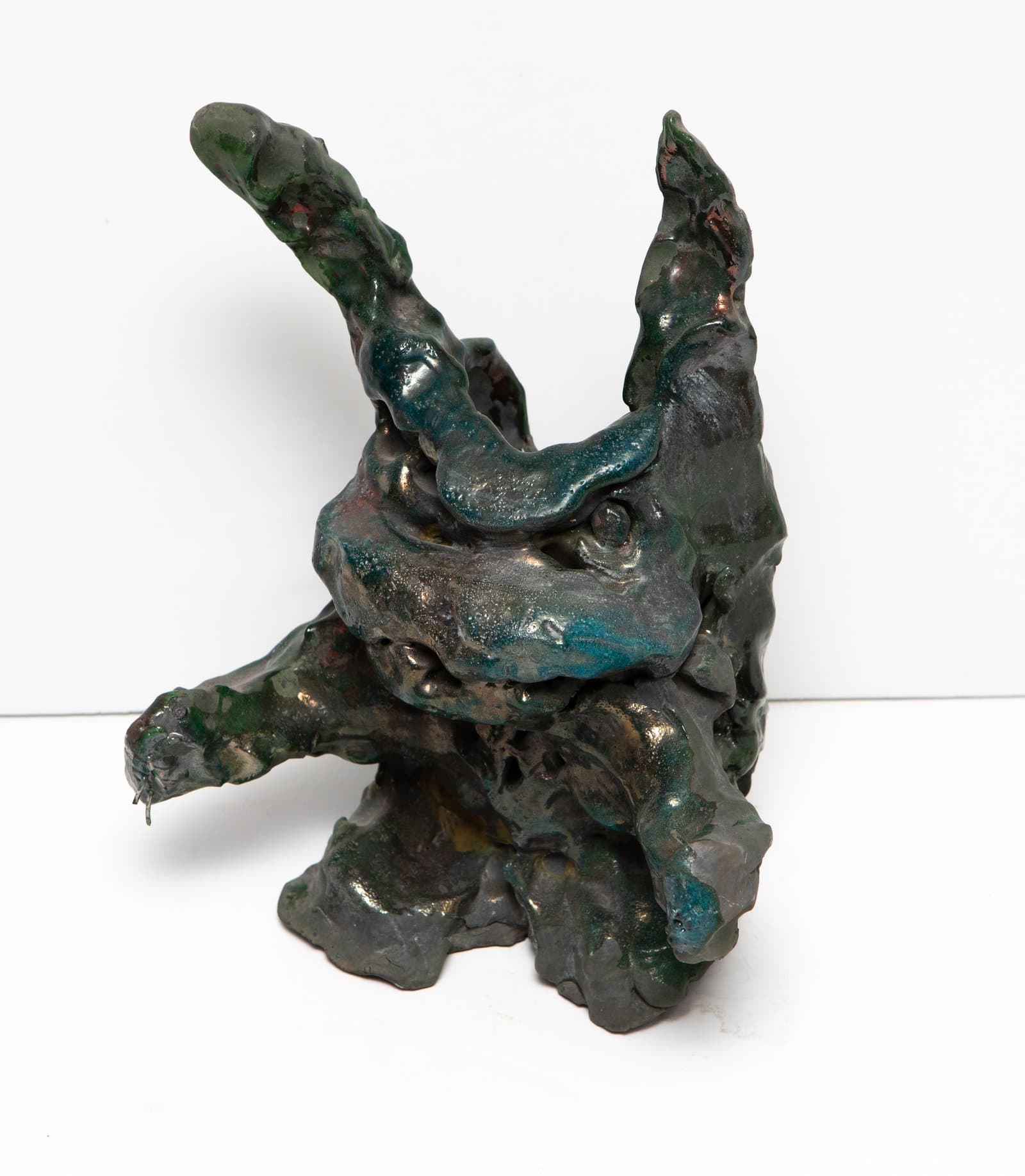 Ceramic sculpture with irregular, organic form featuring upward-reaching protrusions, glazed in deep teal, green, and bronze tones.
