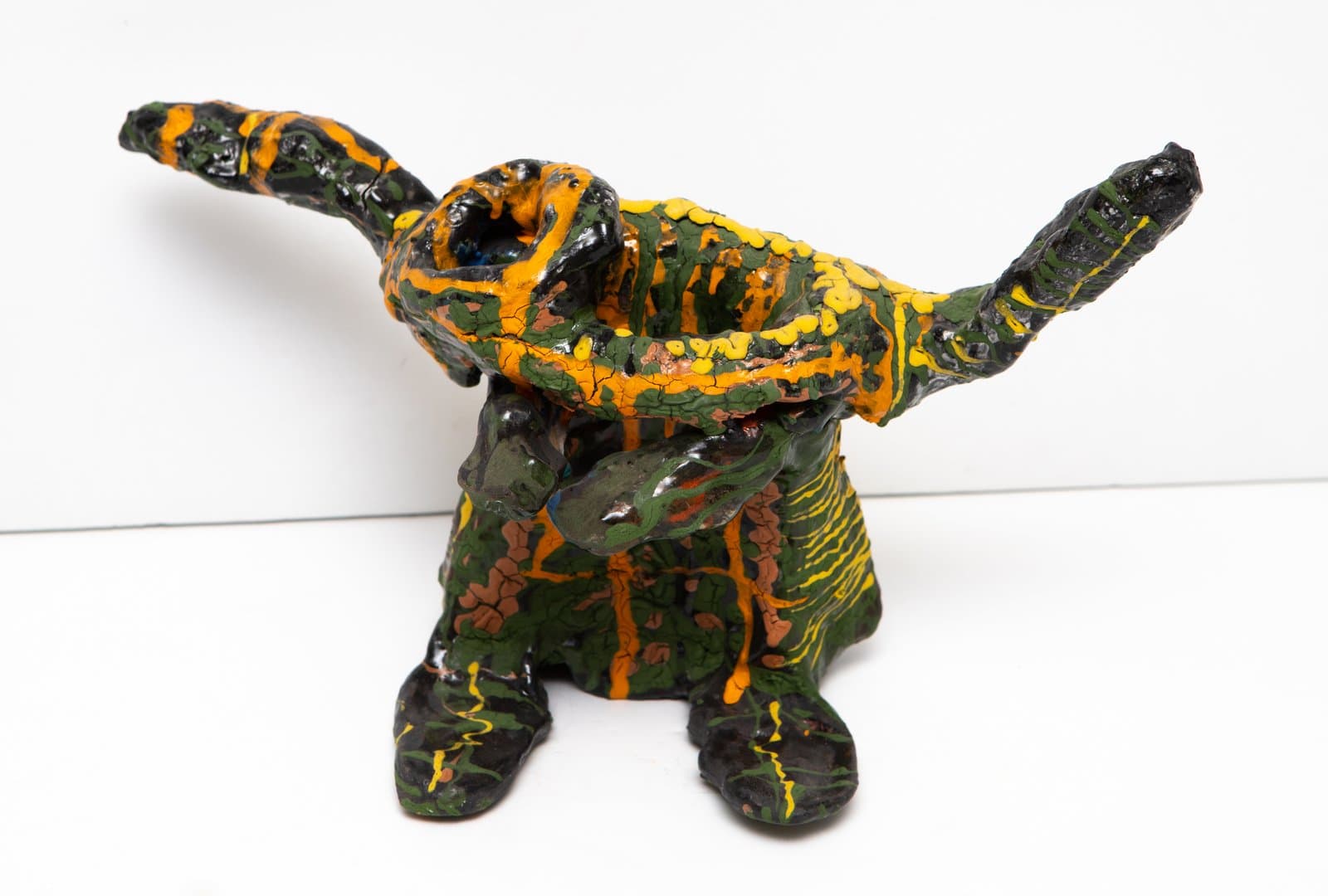 Ceramic sculpture of a squat animal figure with outstretched limbs, glazed in orange, yellow, green, and black.