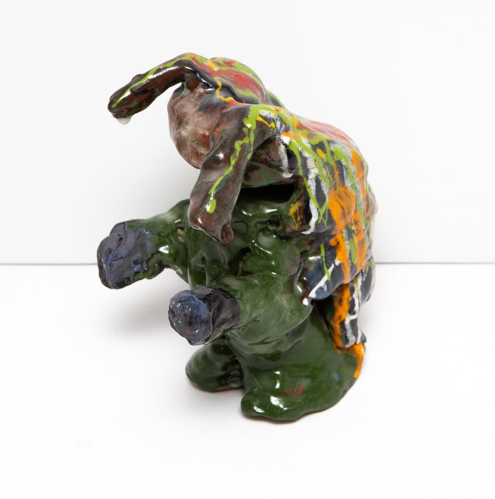 Ceramic sculpture of an abstract crouching figure glazed in green, brown, orange, and yellow with dripping multicolor glaze.