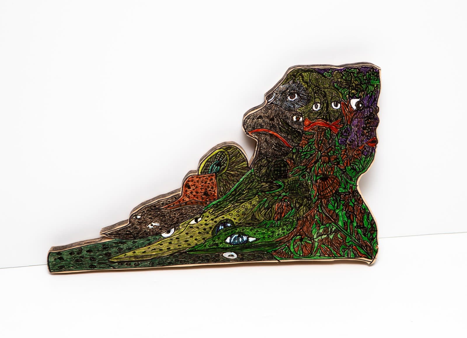 Pen on wood cutout depicting layered animal-like faces in dense green, brown, purple, and orange patterns.