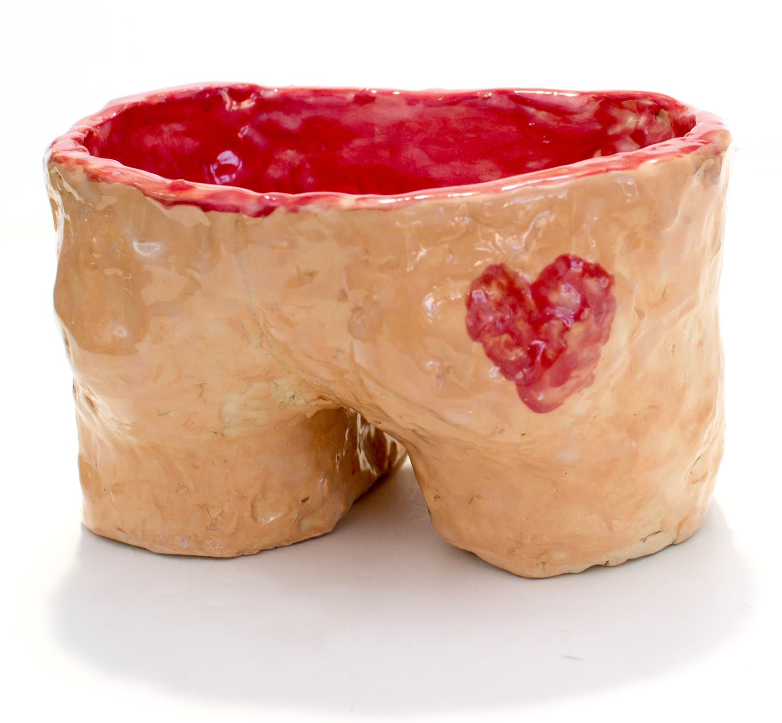Hand-built ceramic bowl shaped like a pair of buttocks, glazed in peach with a vivid red interior and a small red heart motif.