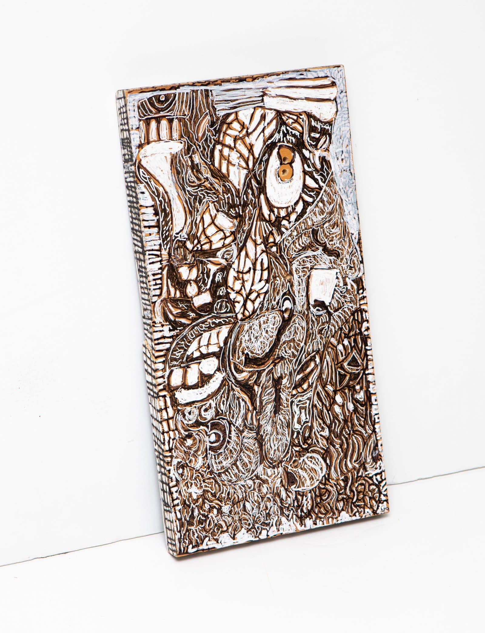 Rectangular wood relief sculpture densely carved and painted with interlocking organic forms in brown, white, and black.