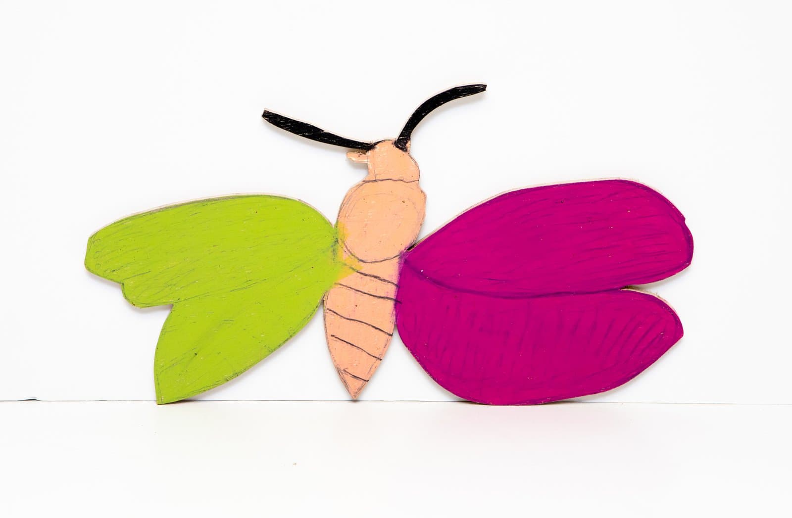 Cut-out wood butterfly with lime green left wings, magenta right wings, peach body, and black antennae, colored with Prismastix.