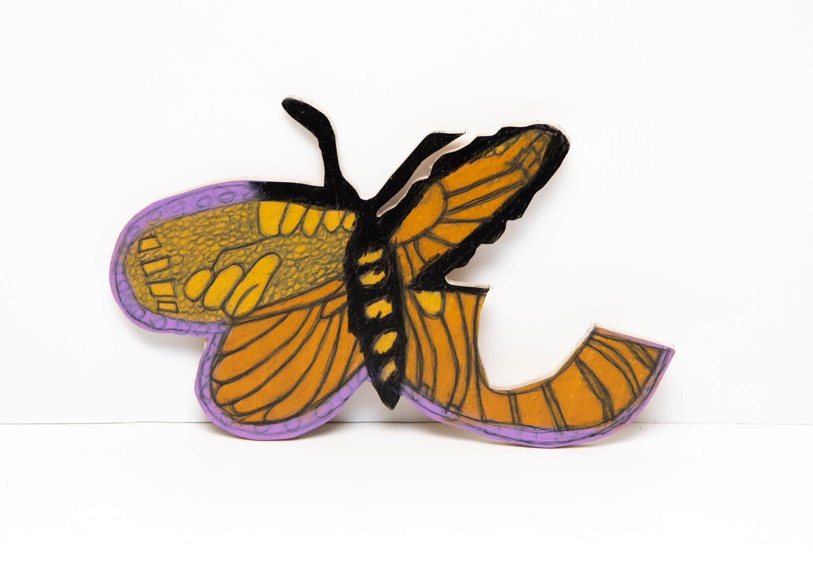 Cutout wood sculpture of a butterfly with asymmetrical wings in orange, yellow, black, and purple, drawn with colored pencil.