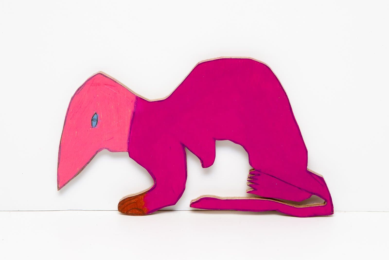 Cut wooden silhouette of a crouching pink and magenta figure with a single blue eye, painted with Prismastix on wood.