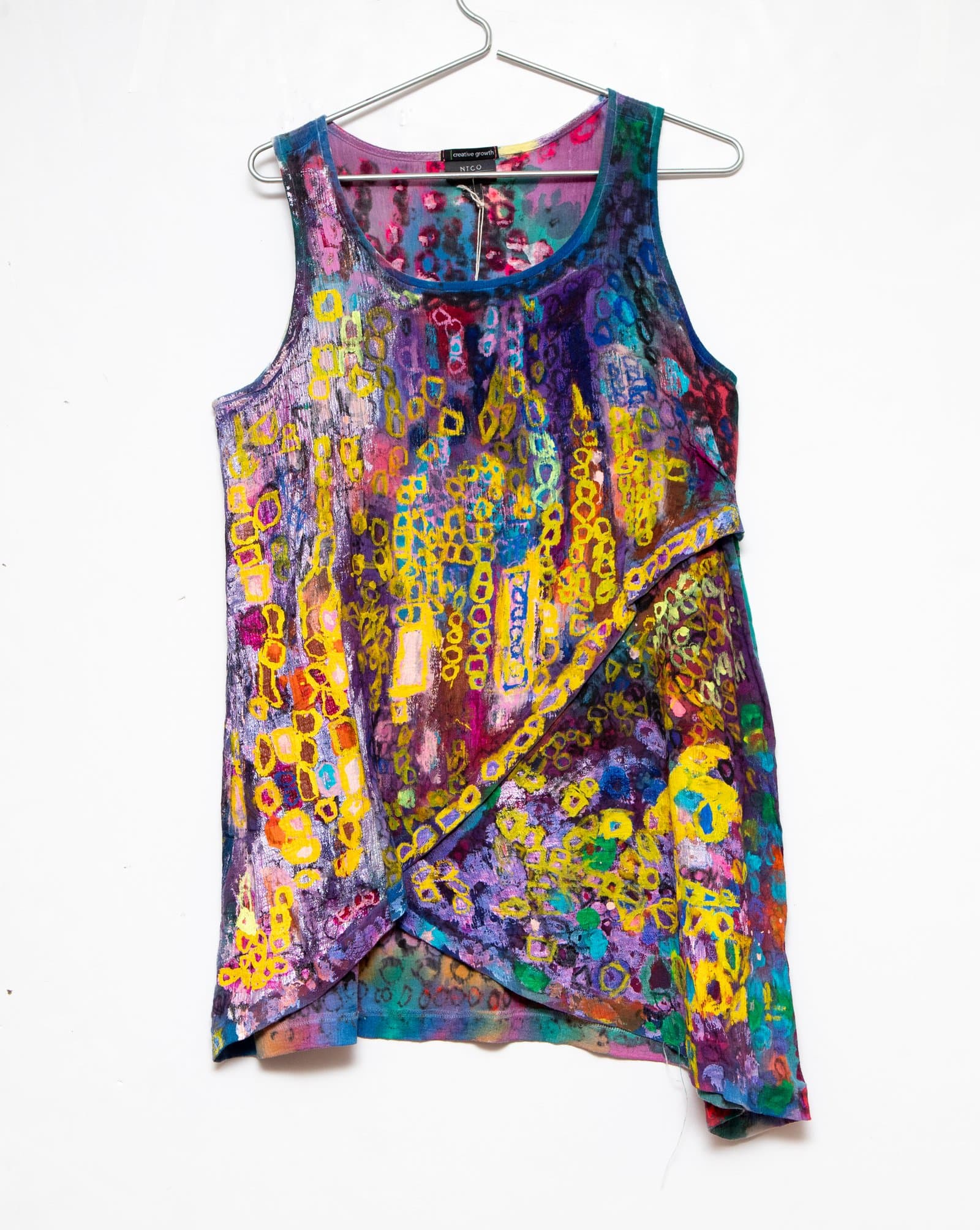 Hand-painted sleeveless fabric top on a metal hanger, covered in yellow chain-link rings on a purple and multicolor ground.