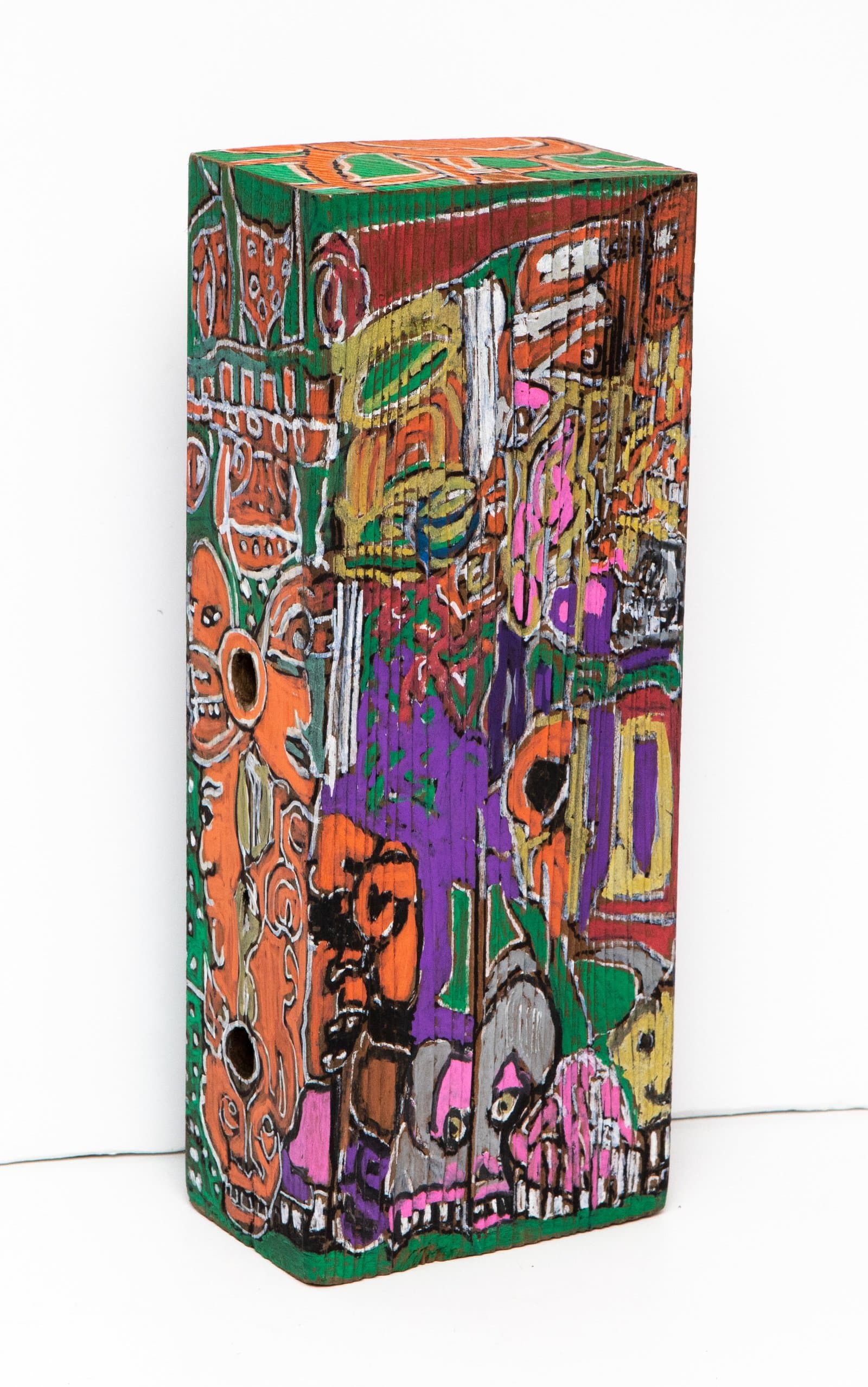 Painted wood block sculpture covered in dense acrylic imagery in orange, green, purple, and pink on all visible surfaces.
