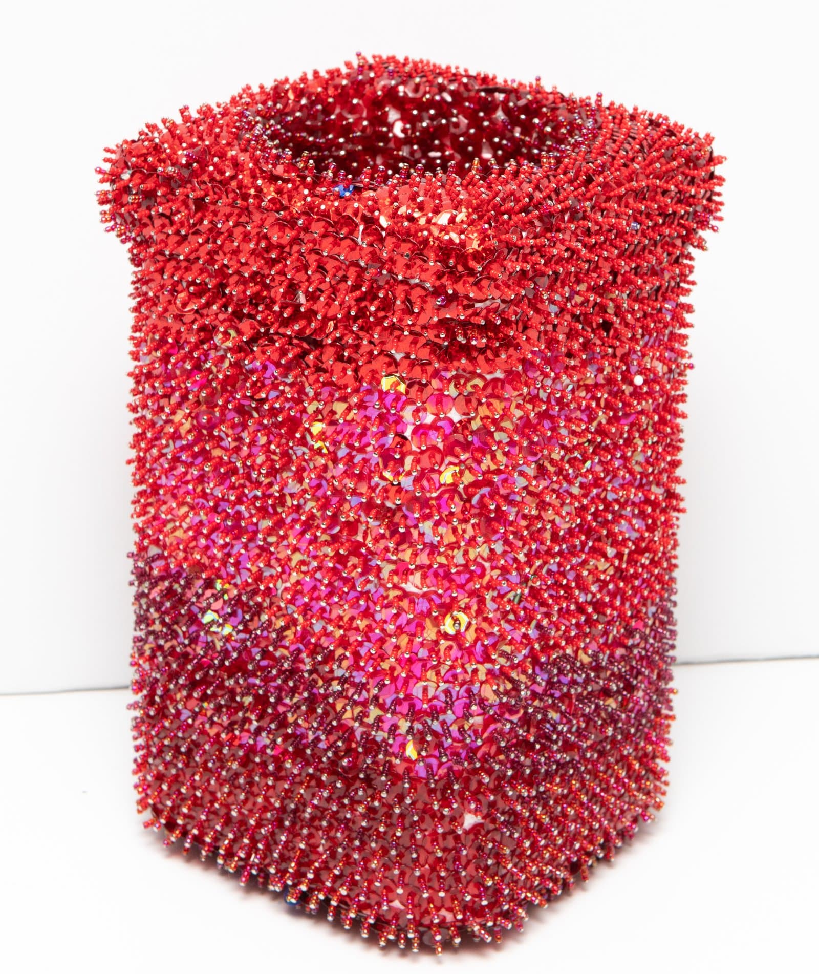 Cylindrical sculpture densely covered in red sequins and seed beads, iridescent pink and magenta tones, against white background.